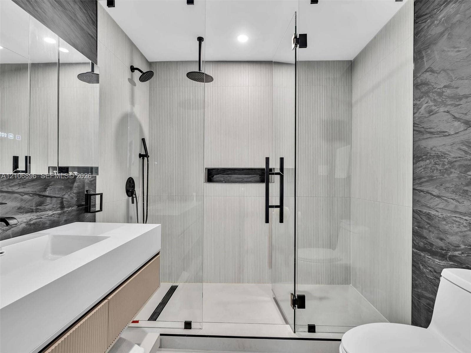 Bathroom featuring a floating vanity with integrated sink, walk-in shower with frameless glass enclosure, dual shower heads including a ceiling-mounted rainfall fixture, and recessed wall niche
