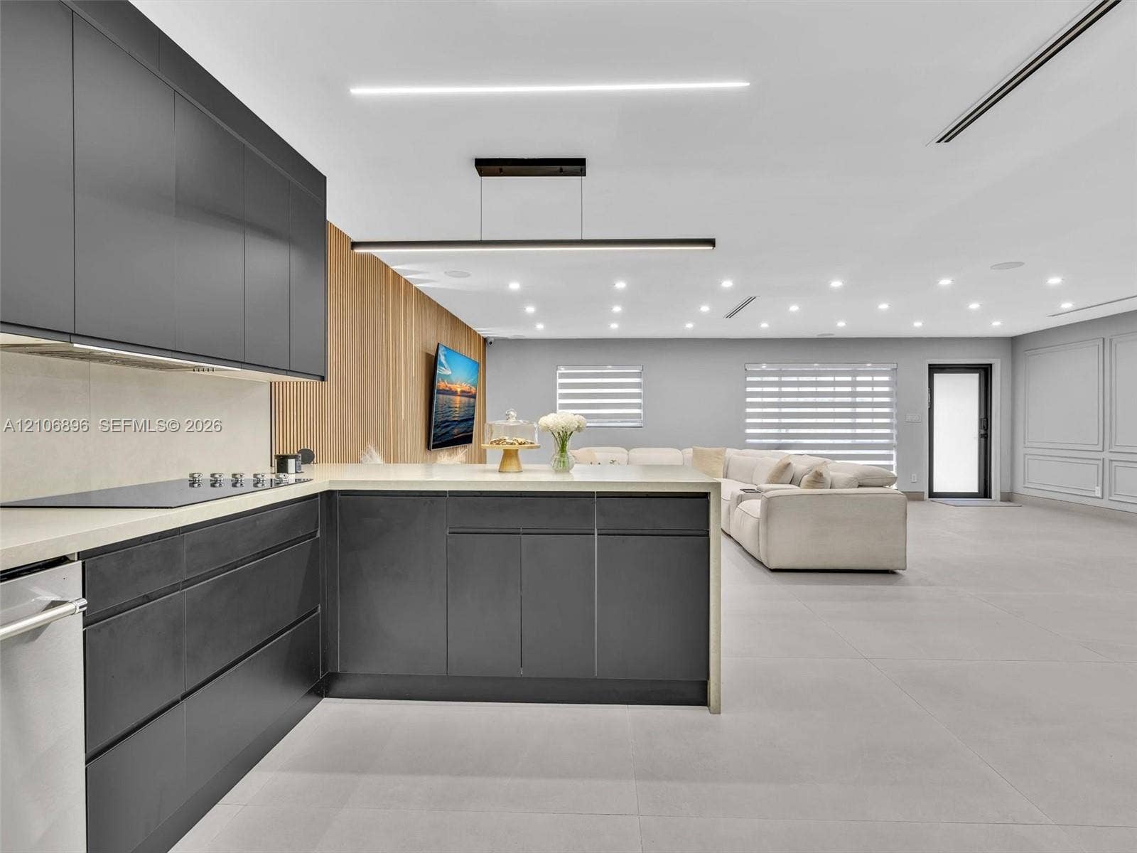 Contemporary kitchen featuring flat-panel charcoal cabinetry, light-toned stone countertops, linear pendant lighting, wood-slat accent wall detailing, and large-format tile flooring