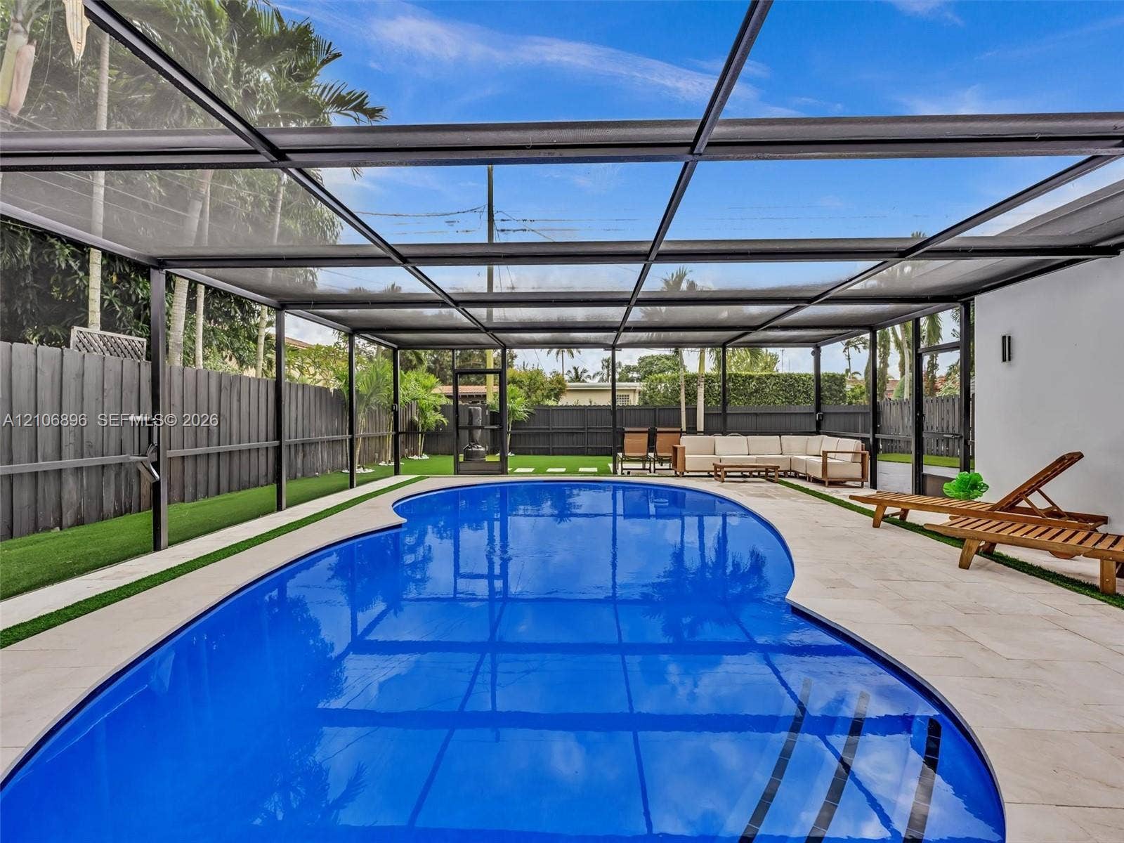 Screened-in outdoor living area featuring a custom-shaped swimming pool, paved pool deck, and synthetic turf lawn bordered by perimeter fencing