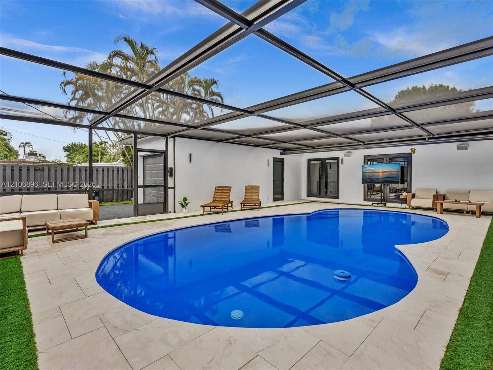 Screen-enclosed pool area with stone tile decking, synthetic turf accents, and perimeter fencing