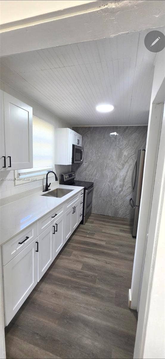 Kitchen featuring white shaker-style cabinetry, solid-surface countertops, wood-finish flooring, a large-format stone-patterned backsplash, and a matte black gooseneck faucet