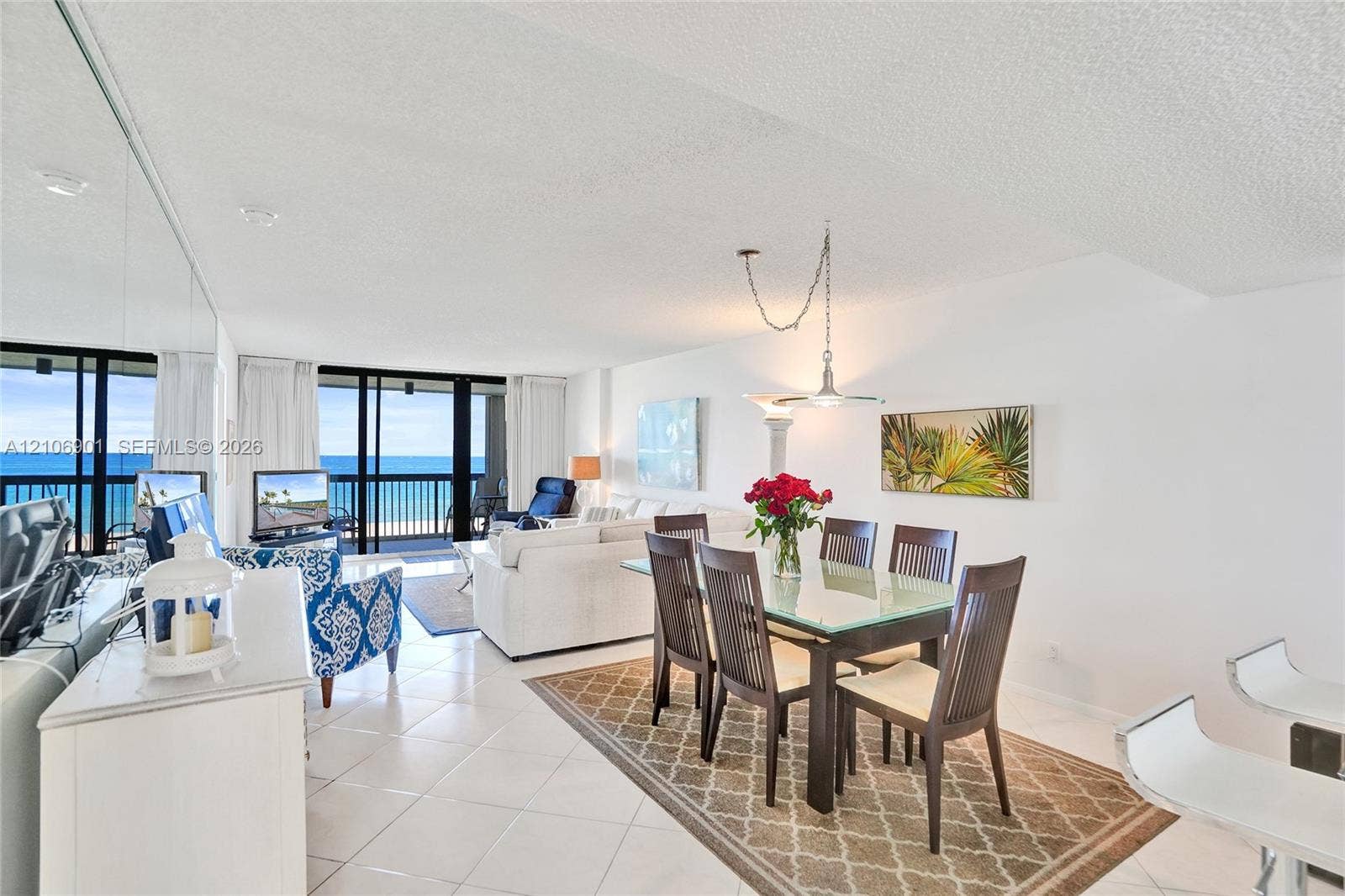 510 N Ocean Boulevard, #308, Pompano Beach, FL 33062 Open-concept interior featuring light-colored floor tiling, mirrored wall paneling, a tiered pendant light fixture, and floor-to-ceiling sliding glass doors opening to a balcony with ocean exposure