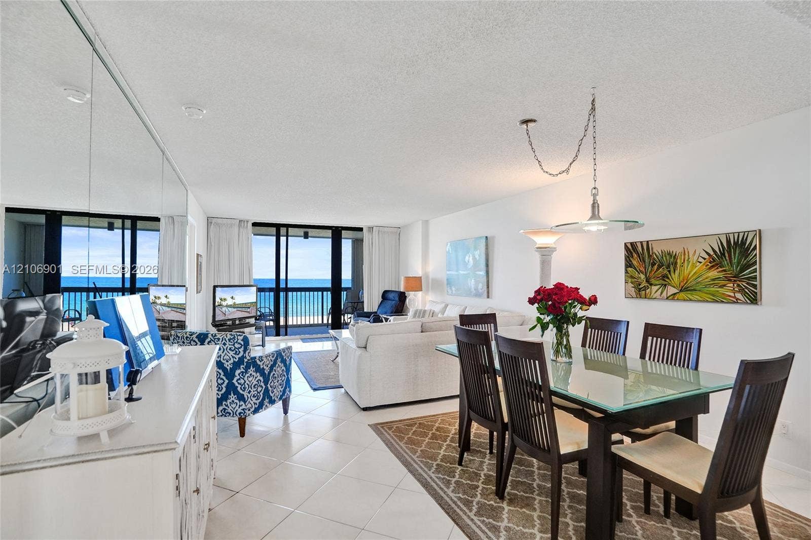 510 N Ocean Boulevard, #308, Pompano Beach, FL 33062 Open-concept area featuring light-toned tile flooring, floor-to-ceiling mirror wall paneling, sliding glass doors, and a suspended metal pendant light fixture