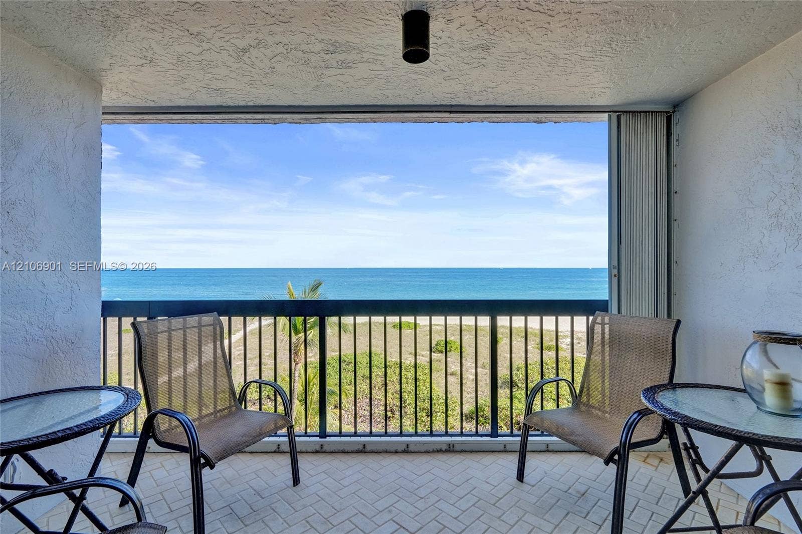510 N Ocean Boulevard, #308, Pompano Beach, FL 33062 Covered balcony featuring herringbone-patterned tile flooring, textured stucco walls, black metal railing, and ocean horizon backdrop