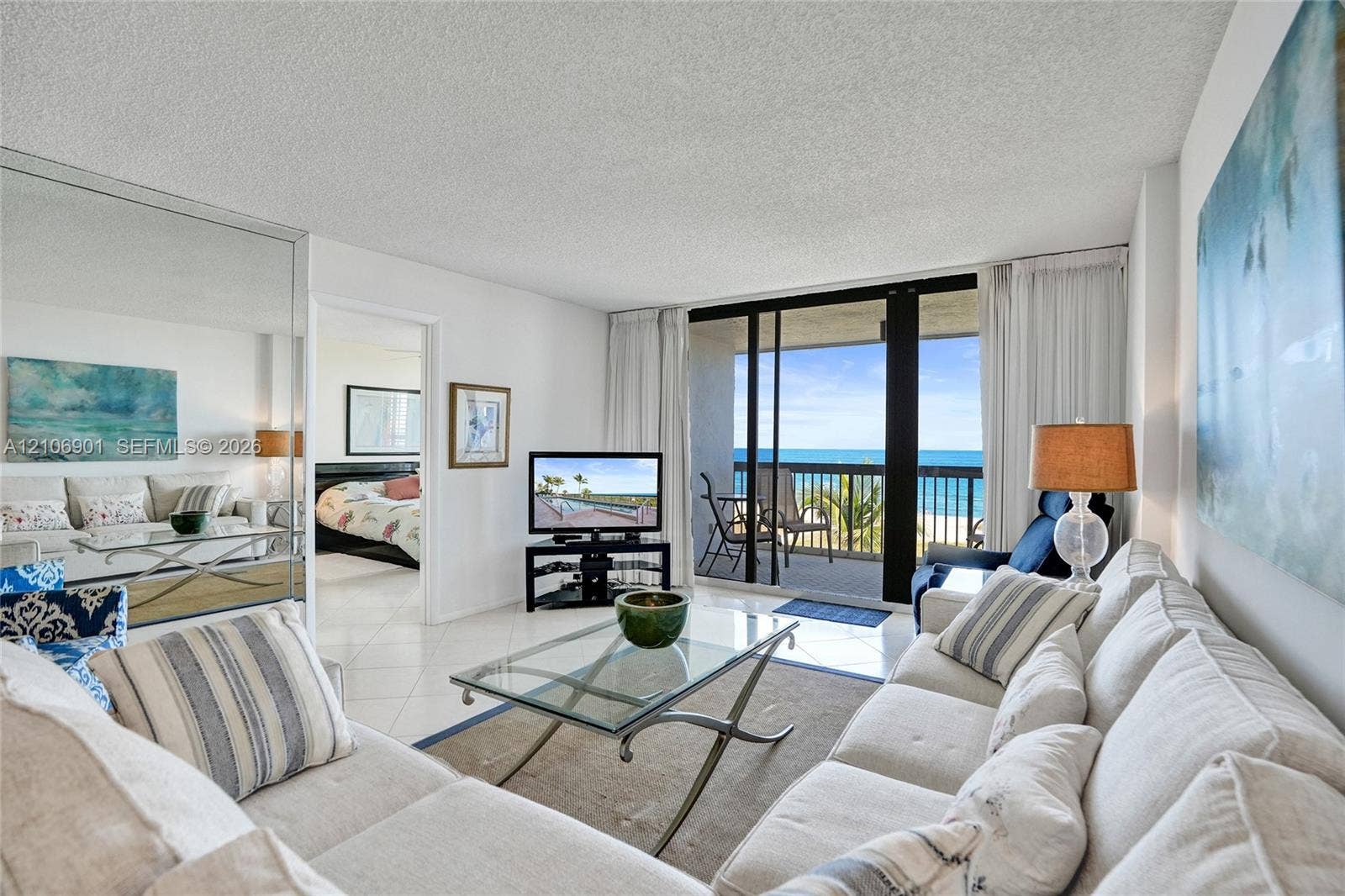 510 N Ocean Boulevard, #308, Pompano Beach, FL 33062 Living area featuring tile flooring, floor-to-ceiling mirrored walls, and sliding glass doors opening to an outdoor balcony with ocean scenery