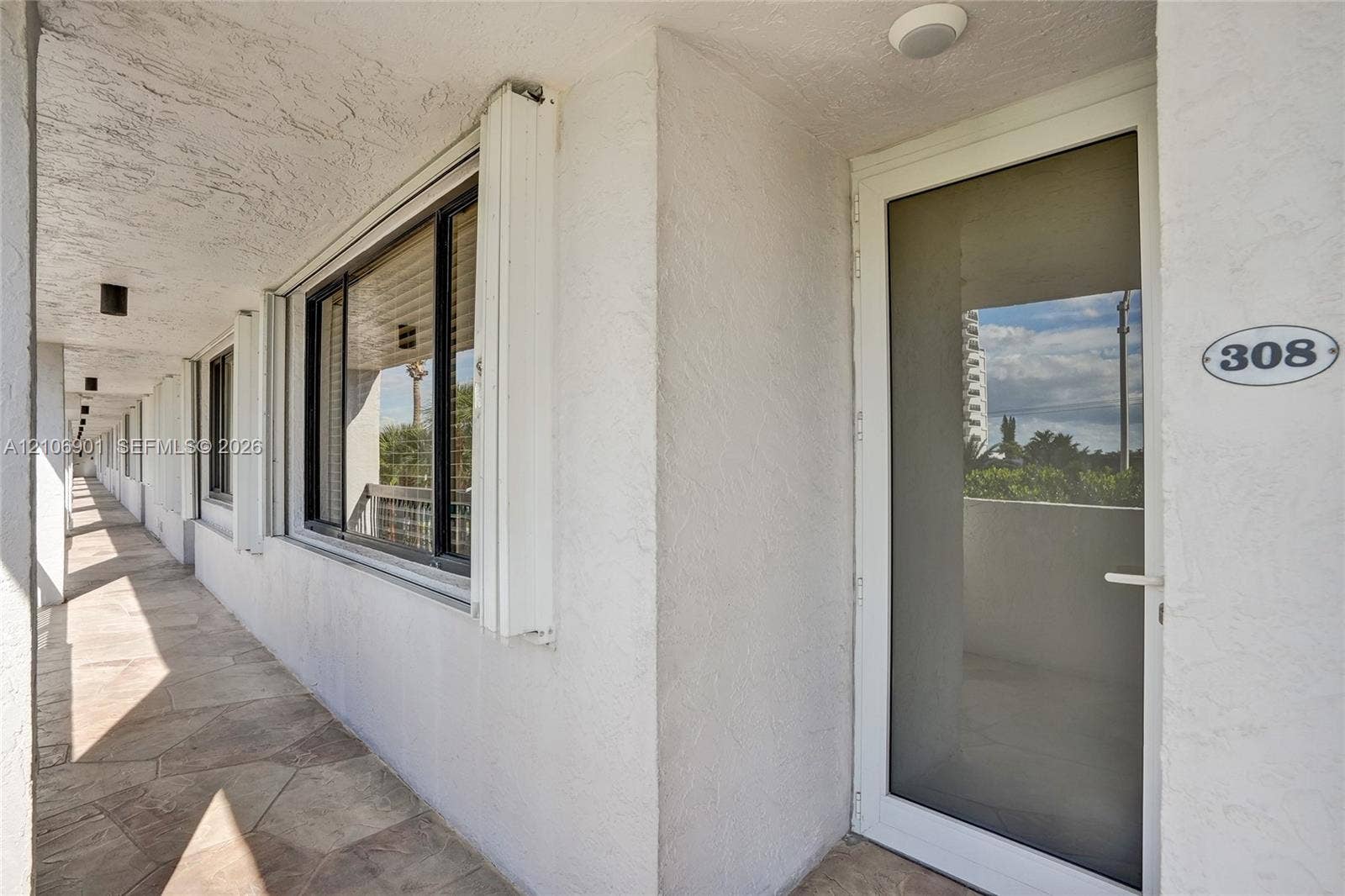 510 N Ocean Boulevard, #308, Pompano Beach, FL 33062 Exterior entry featuring a full-length glass storm door, textured white stucco walls, stone-finish tile flooring, and flush-mount exterior lighting