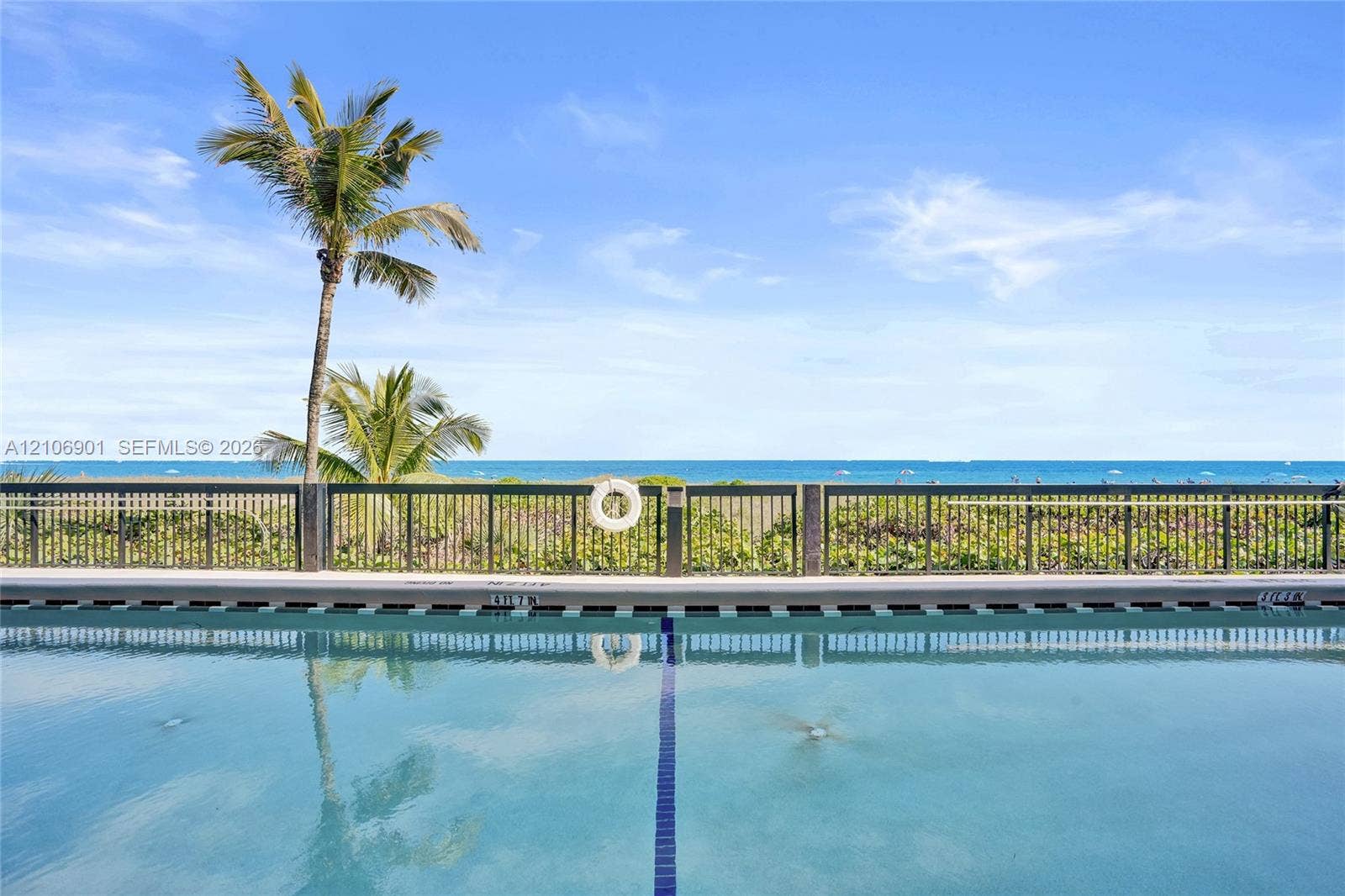 510 N Ocean Boulevard, #308, Pompano Beach, FL 33062 Swimming pool with a lane marker, metallic perimeter fencing, and coastal backdrop featuring palm trees and ocean