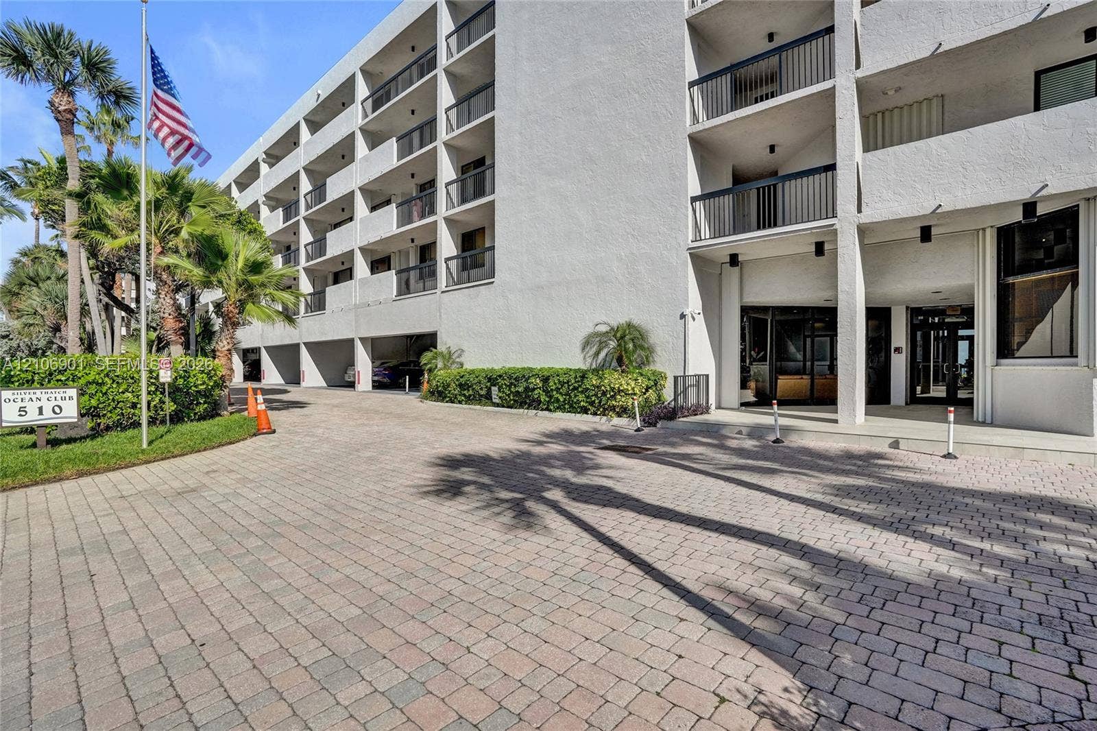 510 N Ocean Boulevard, #308, Pompano Beach, FL 33062 Multi-story concrete exterior with private balconies and metal railings, paver-stone driveway, and manicured tropical landscaping