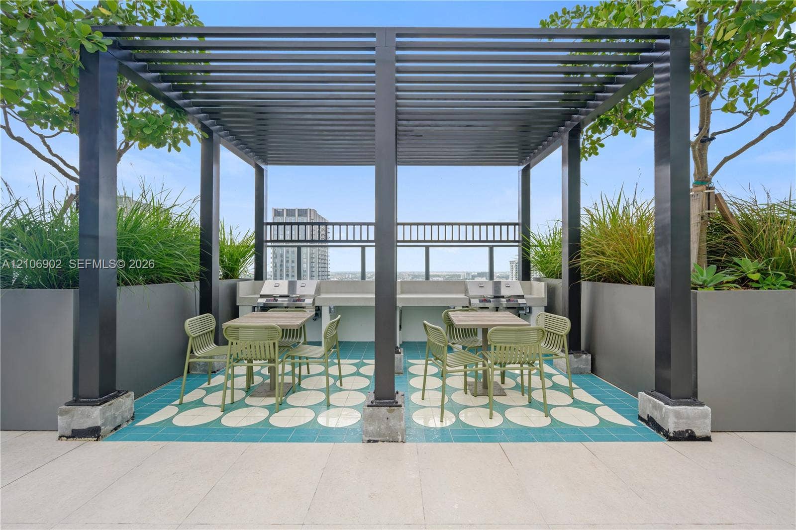 11 NE 6th Street, #1111, Miami, FL 33132 Rooftop terrace featuring a black metal pergola, dual built-in outdoor cooking stations, patterned tile flooring, and integrated metal planters with mature landscaping