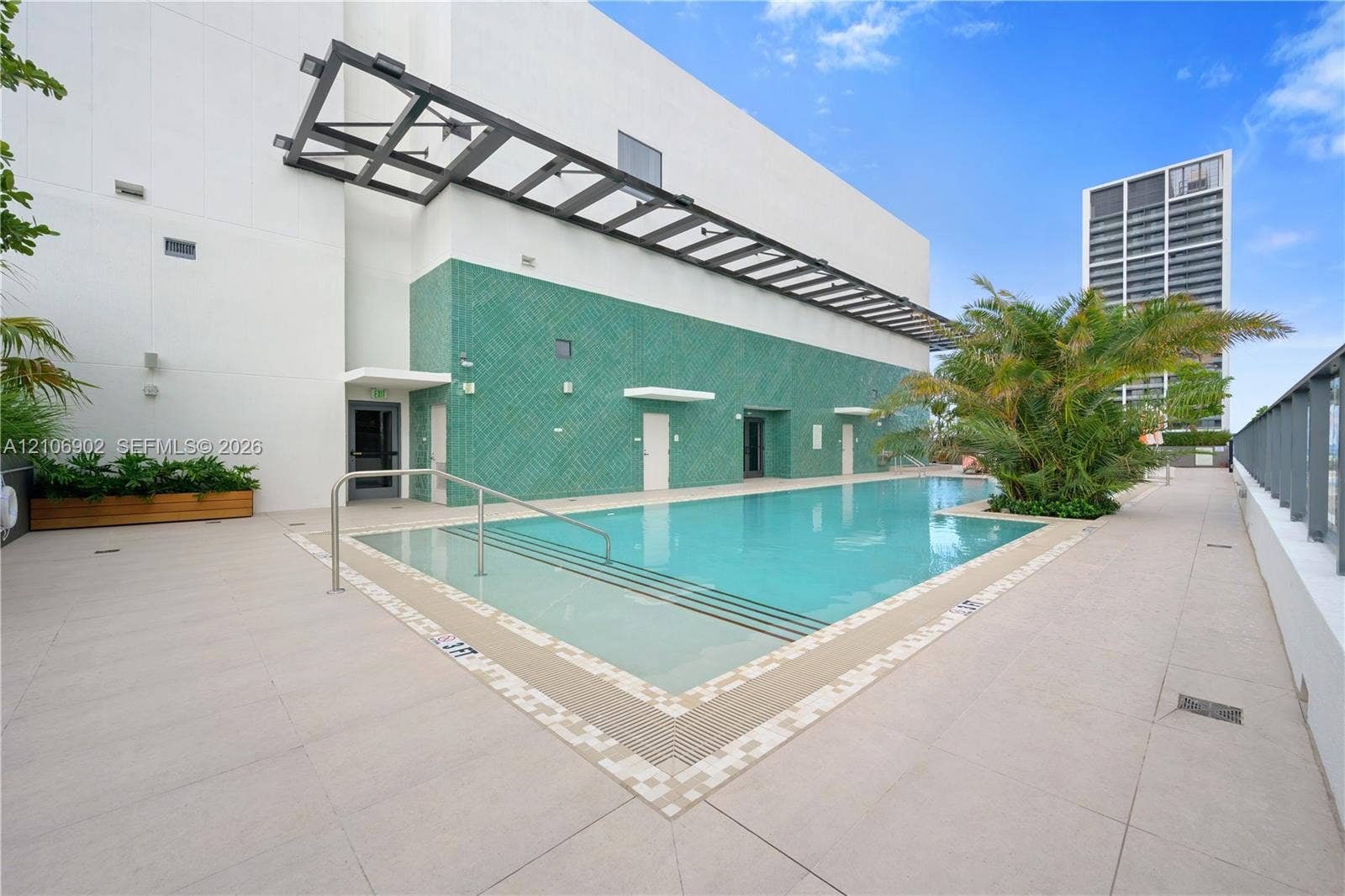 11 NE 6th Street, #1111, Miami, FL 33132 Swimming pool featuring a tiled surround, recessed entry steps, metallic handrail, and green textured accent wall with an overhead architectural pergola