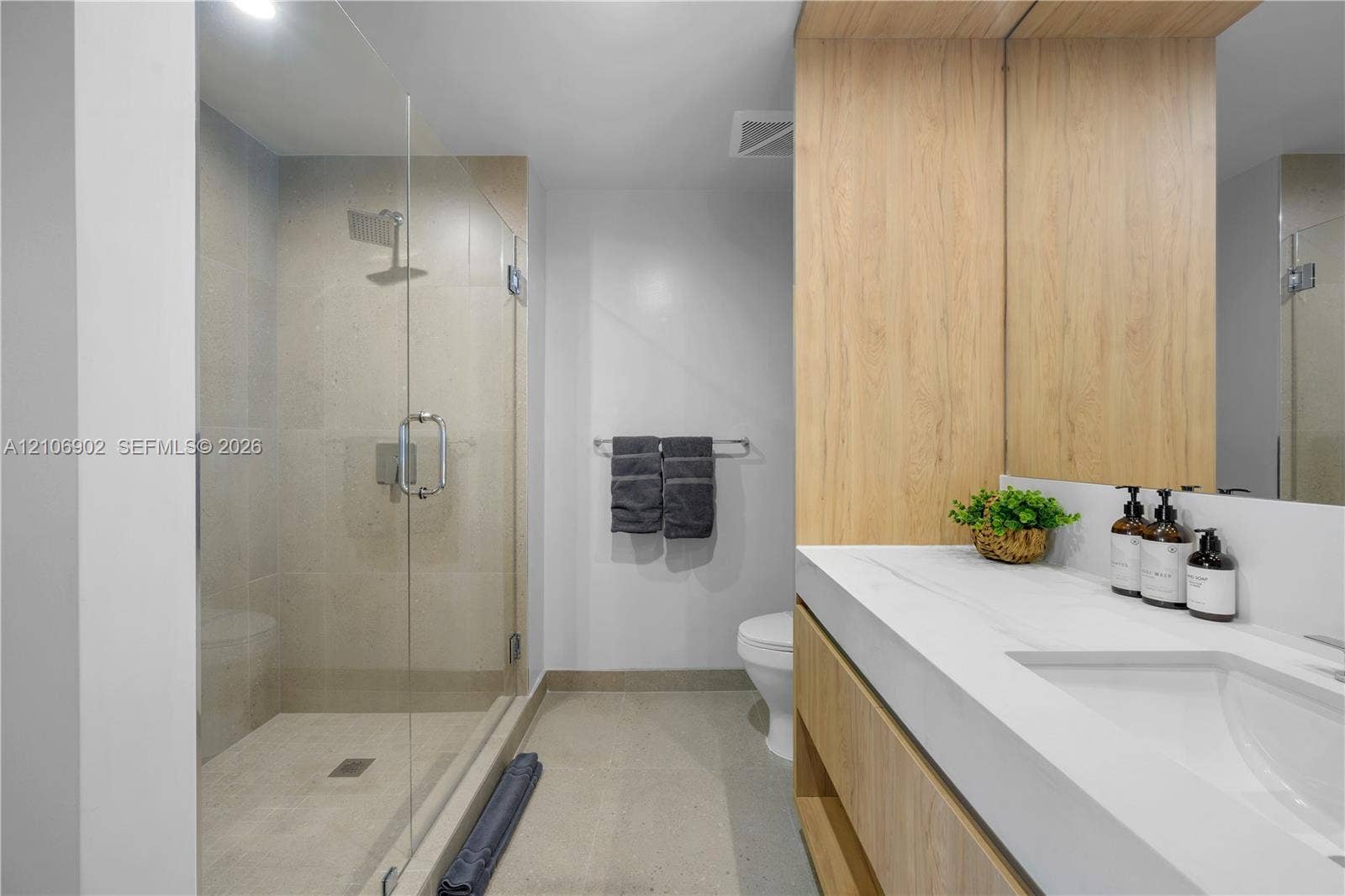 11 NE 6th Street, #1111, Miami, FL 33132 Modern bathroom featuring a wood-finish floating vanity with a white countertop, an integrated rectangular sink, a glass-enclosed shower, and full-wall vanity mirror