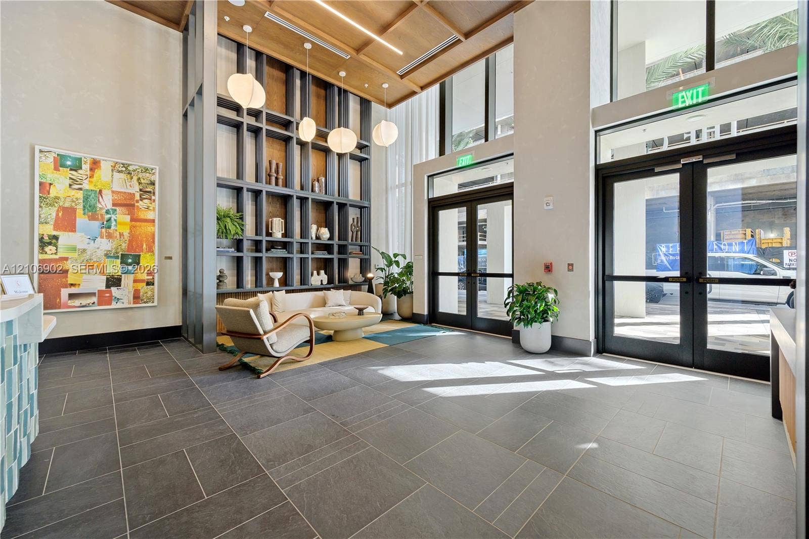 11 NE 6th Street, #1111, Miami, FL 33132 Grand entry featuring large-format tile flooring, double-height ceilings, built-in floor-to-ceiling shelving, recessed wood-slat ceiling detailing, and glass-paneled entry doors