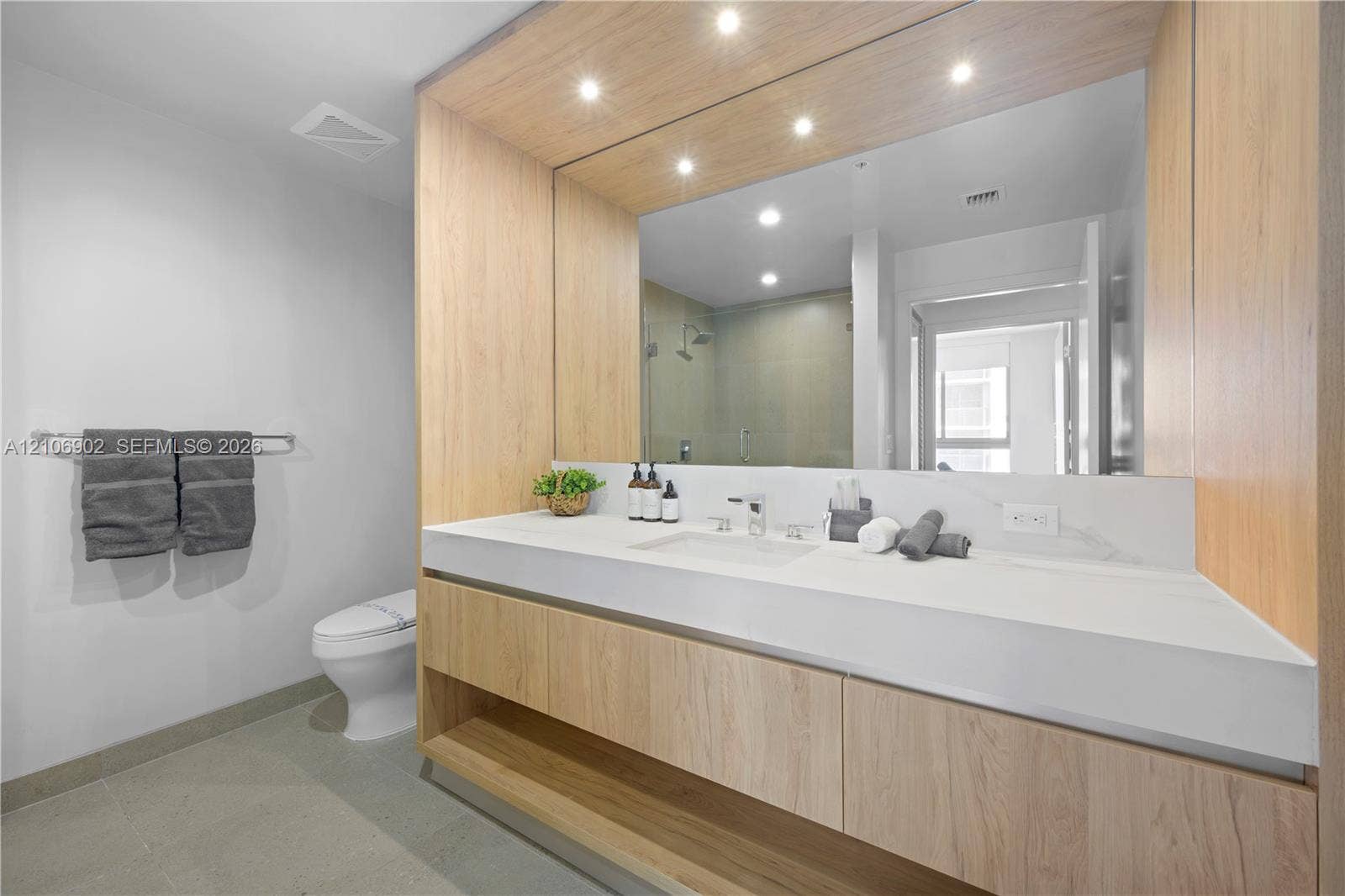 11 NE 6th Street, #1111, Miami, FL 33132 Floating wood-finish vanity with an integrated basin, expansive wall-to-wall mirror, built-in recessed lighting, and large-format tile flooring