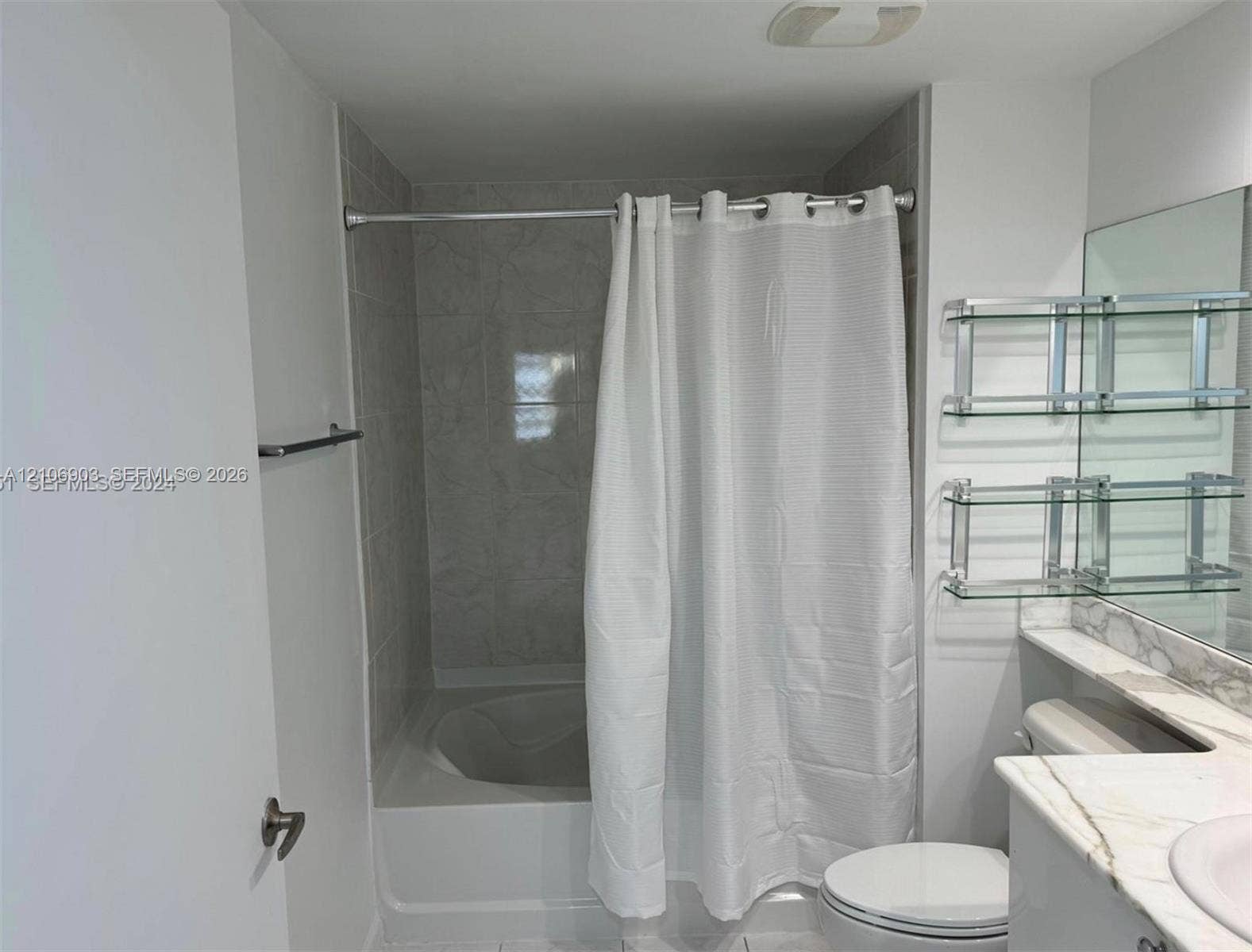 Bathroom featuring a tub-shower combination with tile surround, stone-top vanity, wall-mounted glass shelving, and a large-format mirror