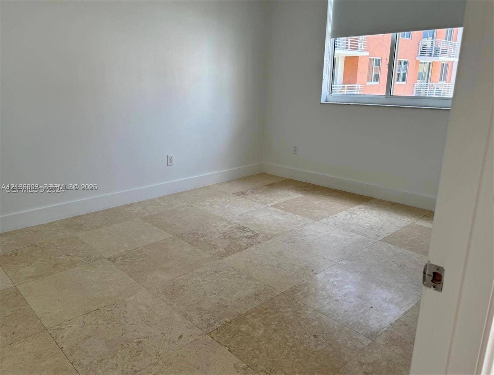 Neutral wall finishes, large-format natural stone tile flooring, and a window with a roller shade