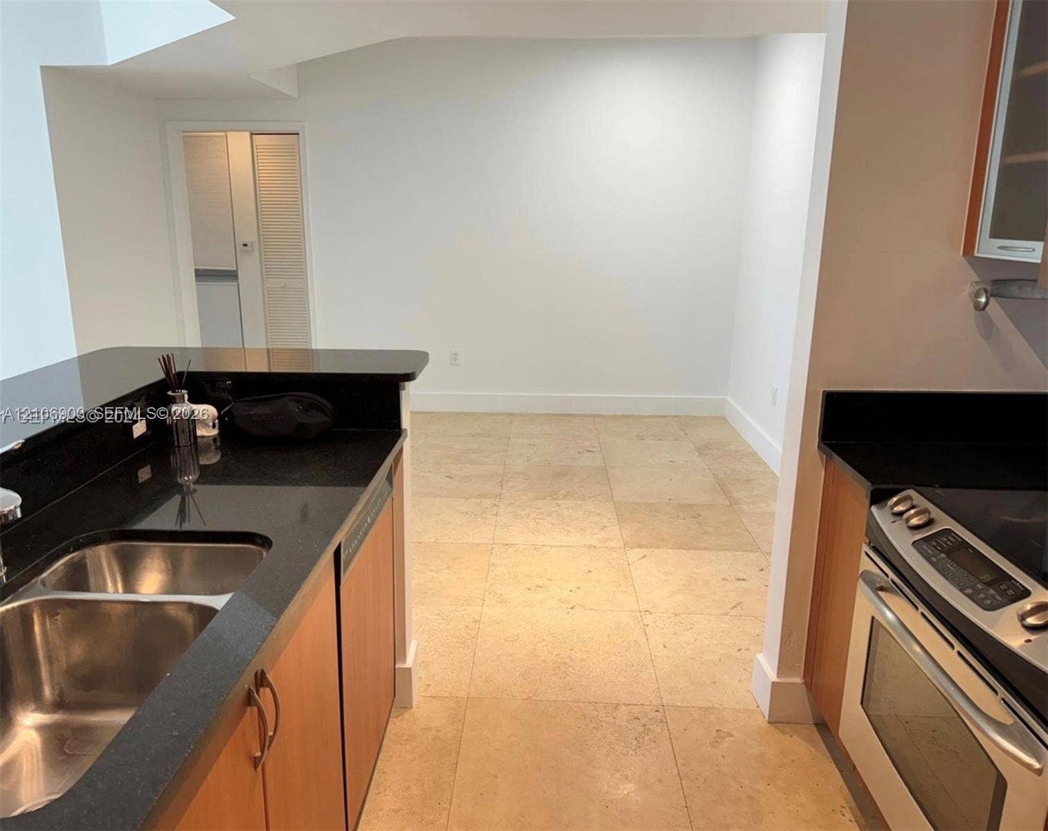 Kitchen featuring dark stone countertops, natural wood-finish cabinetry, stainless steel oven, dual-basin stainless steel sink, and oversized light-toned tile flooring