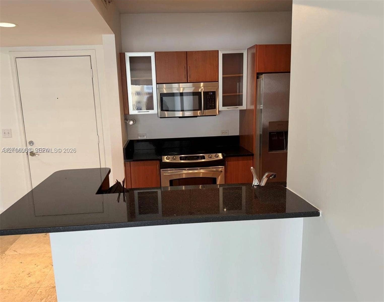 Kitchen featuring flat-panel wood cabinetry, dark stone countertops, stainless steel appliances, and an integrated peninsula breakfast bar