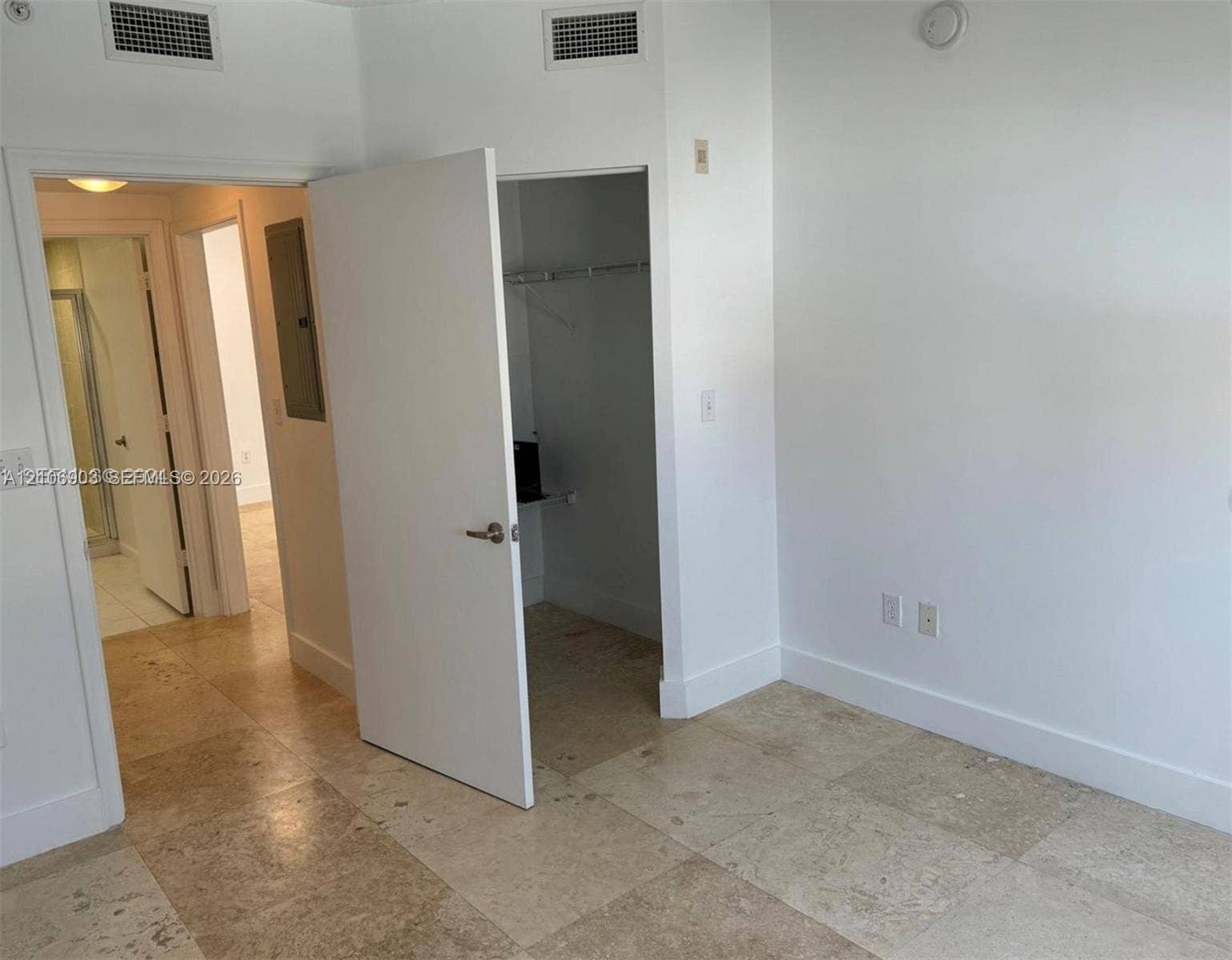Neutral-toned stone flooring throughout, featuring a walk-in closet with integrated shelving, solid-core interior doors, and overhead lighting fixtures
