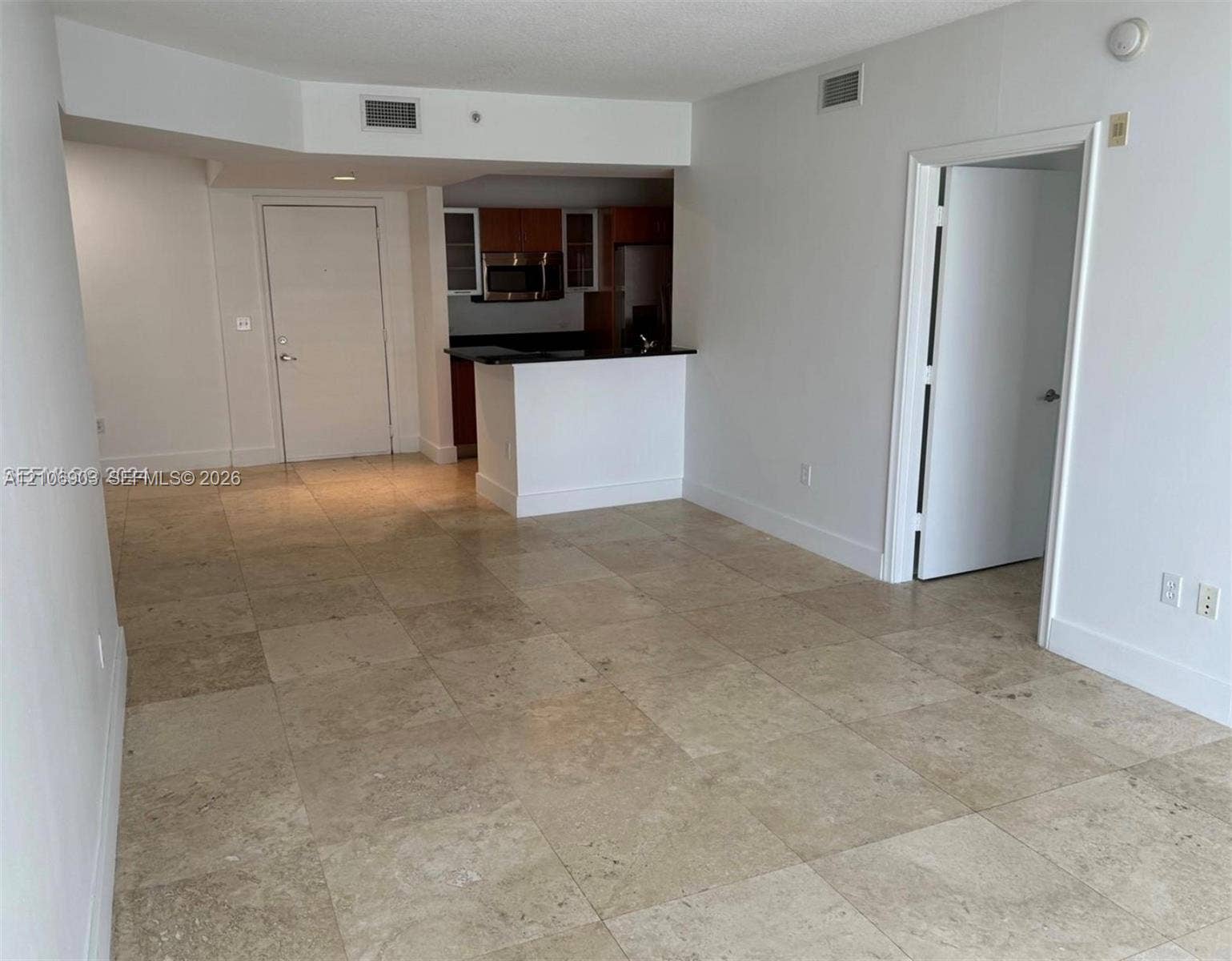Open-concept area featuring large-format stone floor tile and a kitchen with wood-finish cabinetry, black countertops, and built-in stainless steel appliances