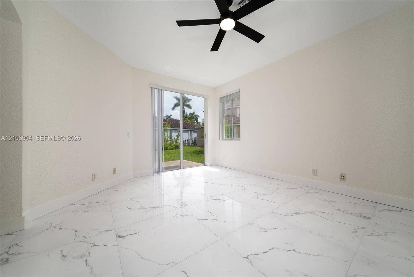 297 Conservation Drive, Weston, FL 33327 Interior space featuring large-format veined tile flooring, neutral wall tones, a black ceiling fan with integrated lighting, and a sliding glass door