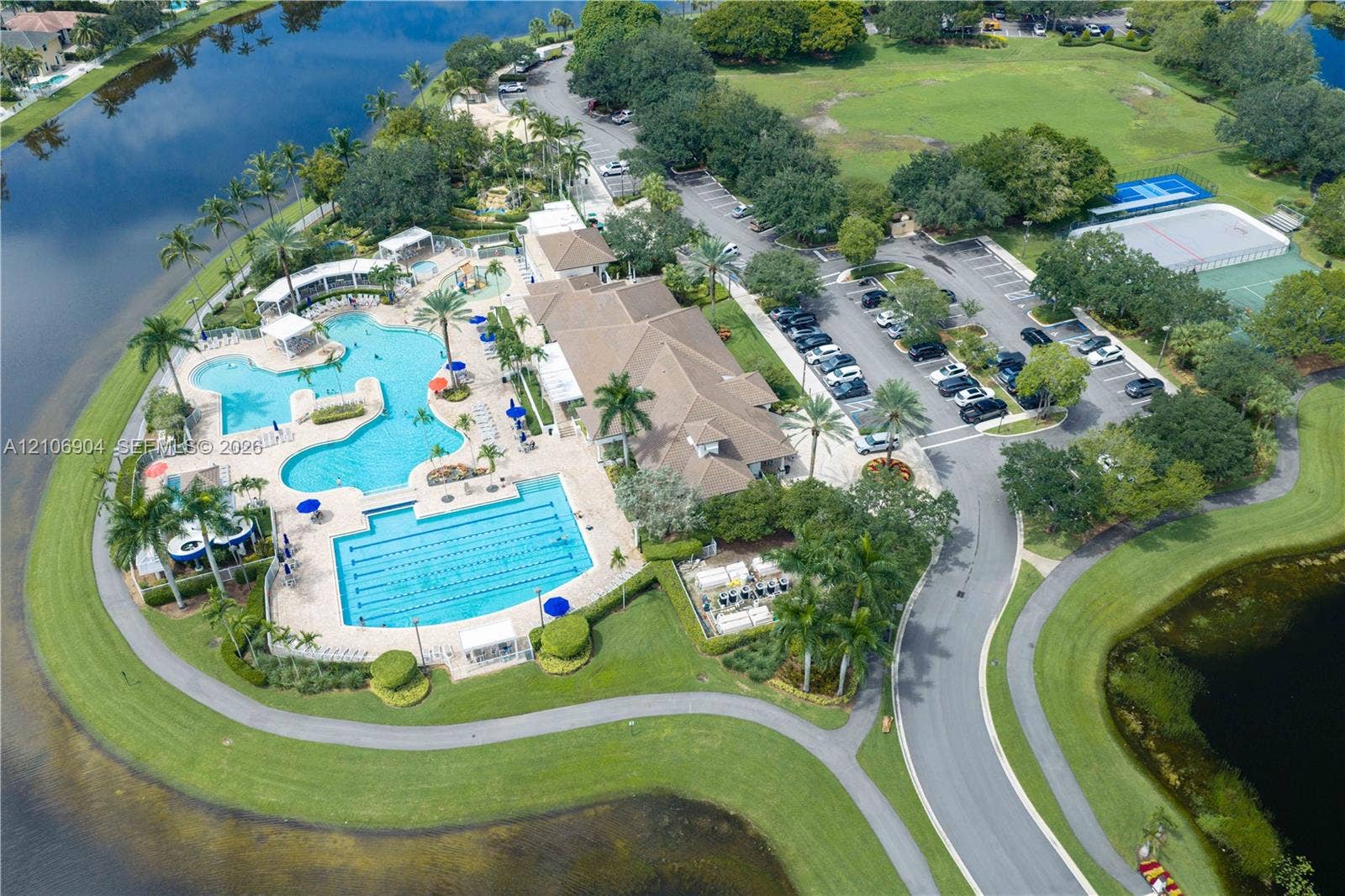 297 Conservation Drive, Weston, FL 33327 Recreational complex featuring multiple swimming pools, paved walking paths, tennis courts, and landscaped grounds situated along a water feature