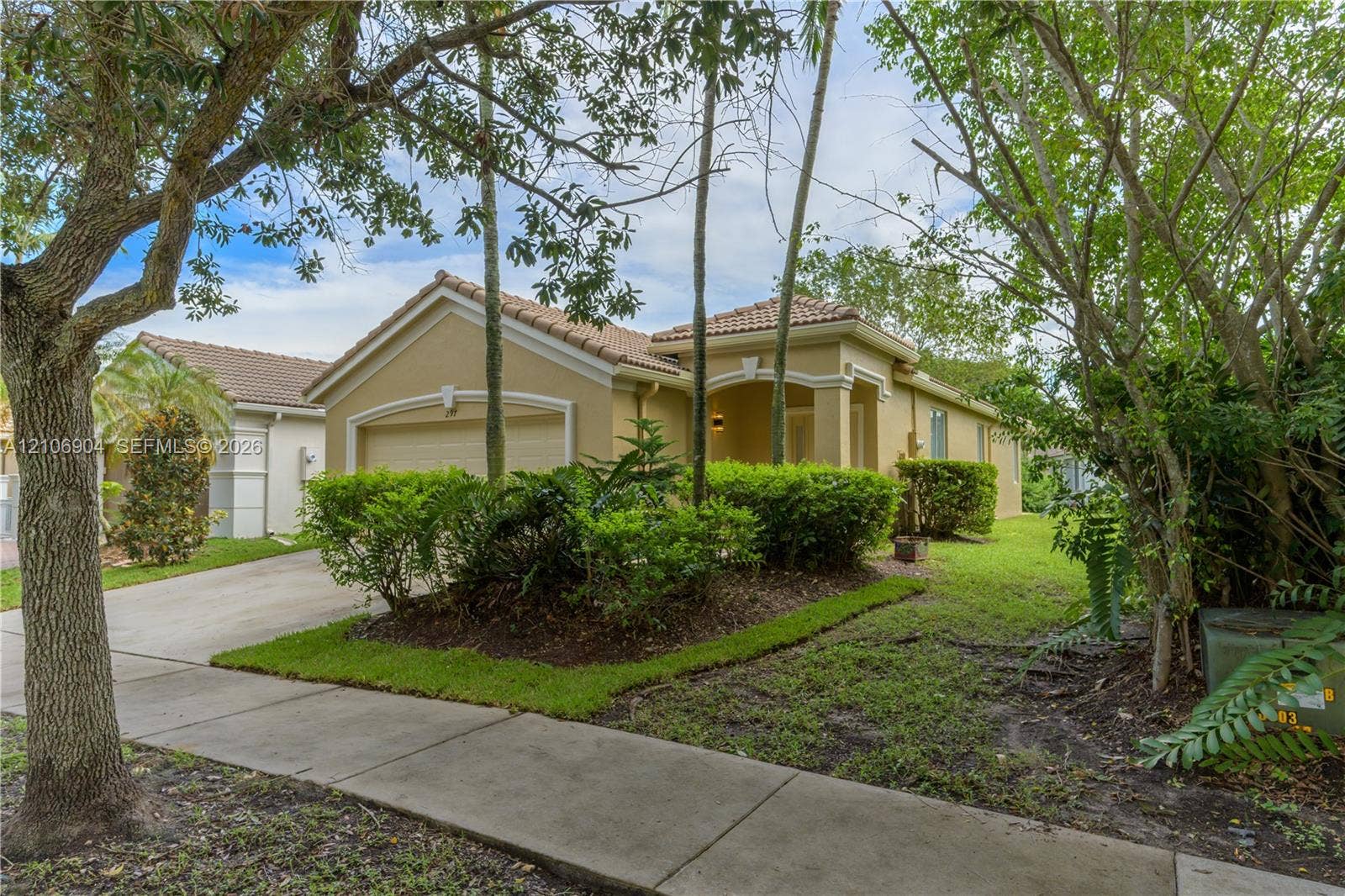 297 Conservation Drive, Weston, FL 33327 Stucco exterior with a tiled roof, arched entryway, and attached garage, complemented by mature landscaping and a concrete driveway