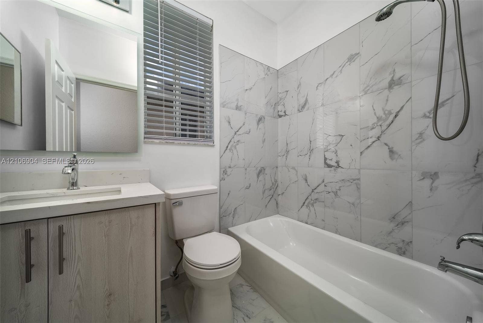 297 Conservation Drive, Weston, FL 33327 Bathroom featuring a shower-tub combination with white and gray veined tile surround, vanity with stone-finish countertop, undermount sink, and wall-mounted mirror