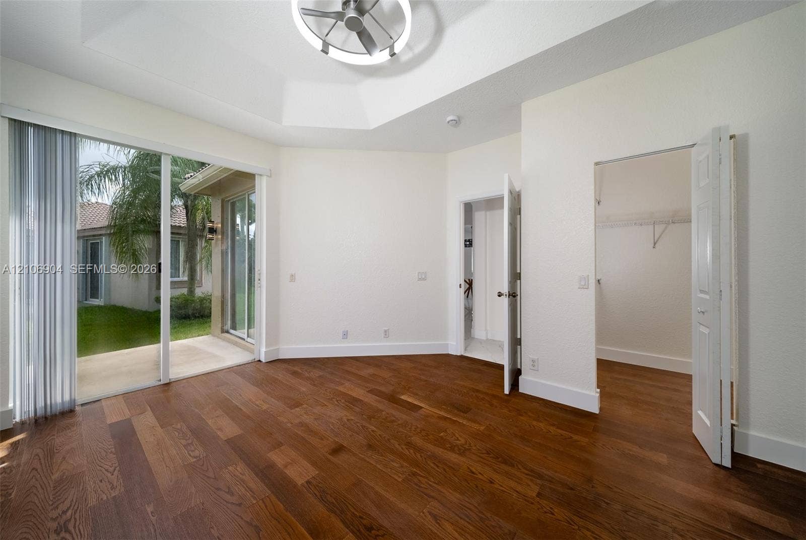 297 Conservation Drive, Weston, FL 33327 Tray ceiling with integrated fan and lighting, wood-finish flooring, sliding glass door, and walk-in closet with wire shelving