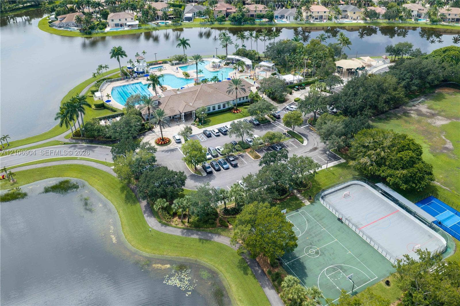 297 Conservation Drive, Weston, FL 33327 Aerial perspective of community facilities featuring a swimming pool, basketball court, tennis court, and waterfront grounds with mature landscaping