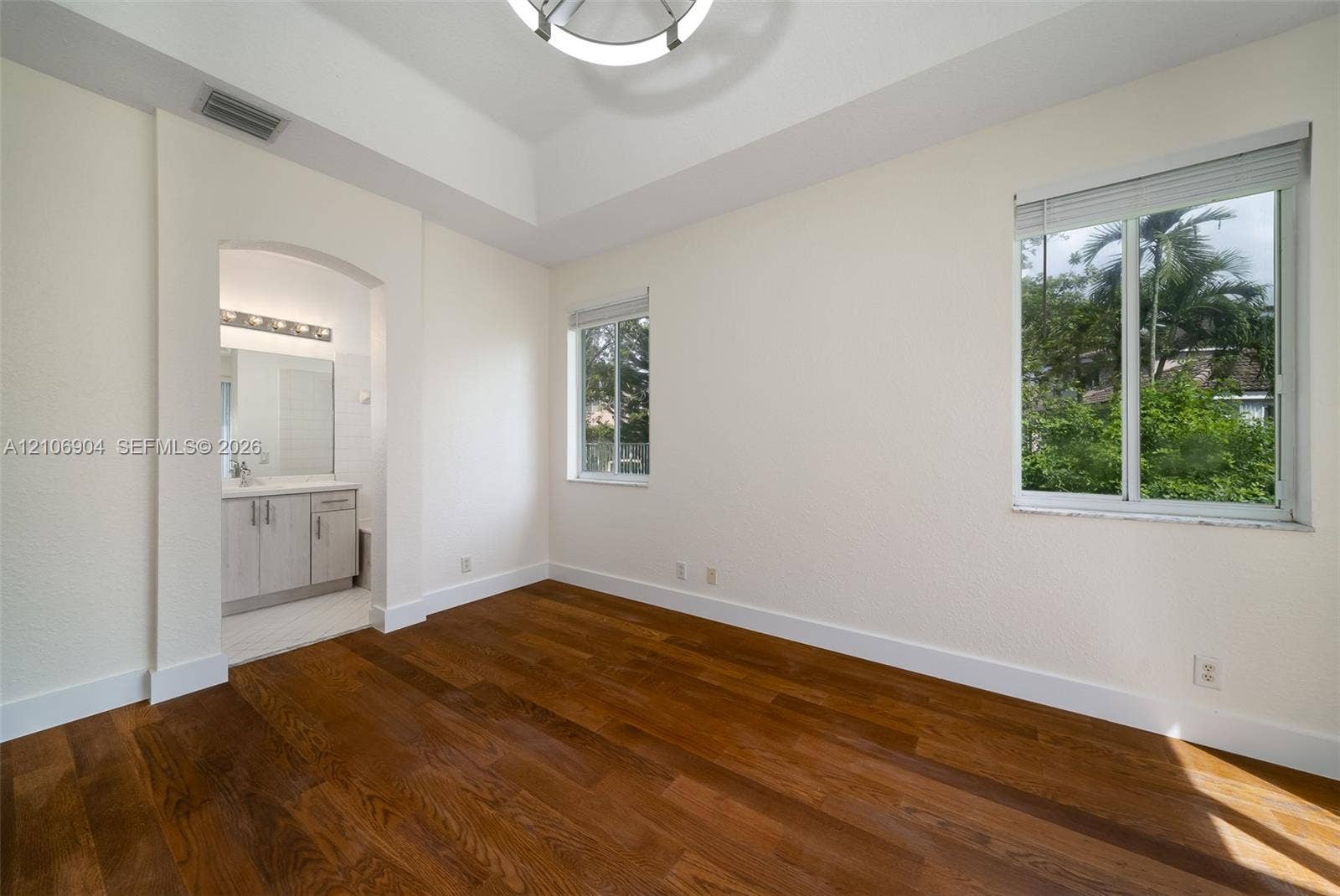 297 Conservation Drive, Weston, FL 33327 Room featuring wood-finish flooring, tray ceiling, arched entryway, and multiple windows with horizontal blinds