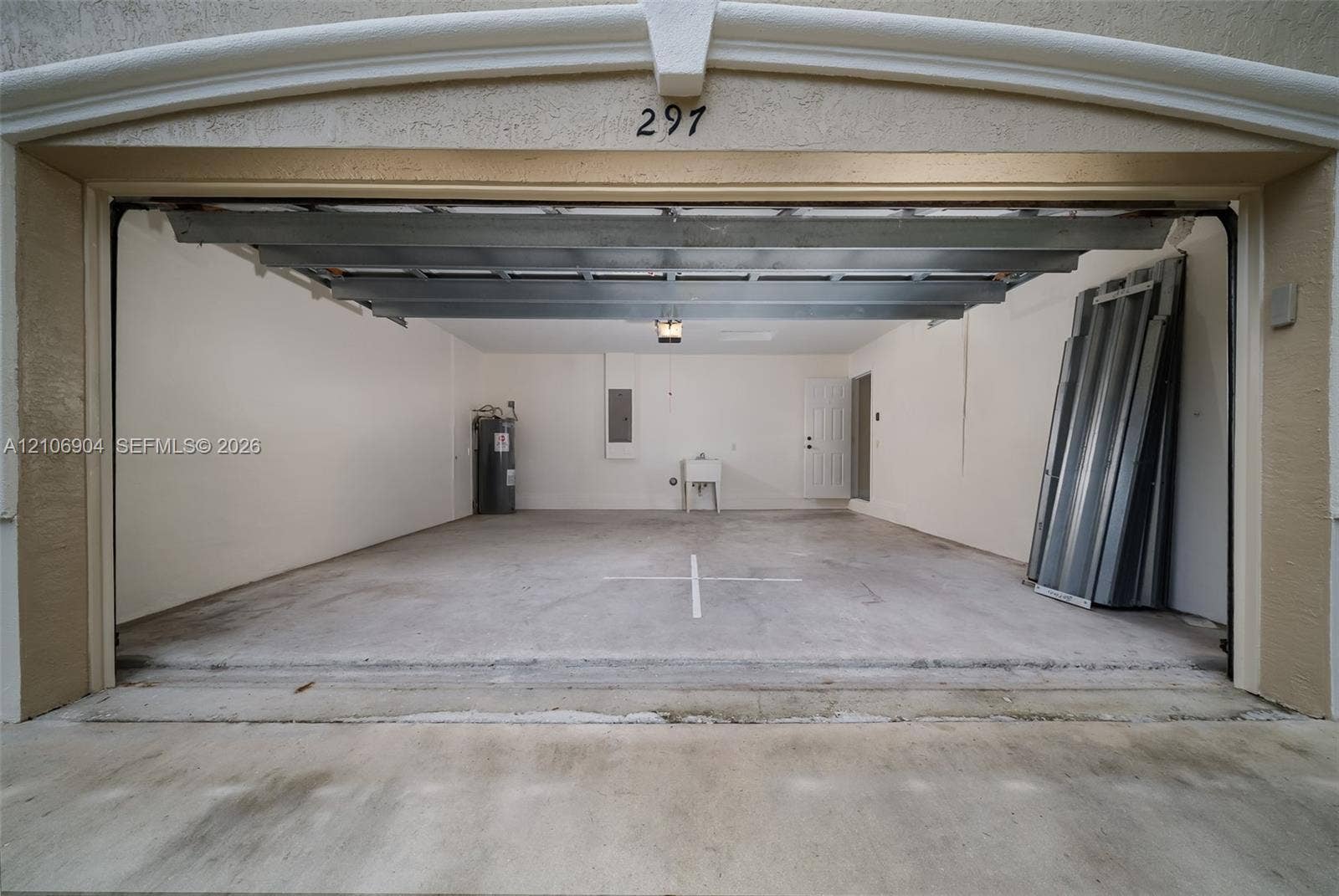 297 Conservation Drive, Weston, FL 33327 Enclosed garage featuring a concrete floor, integrated utility sink, overhead lighting, and dedicated water heater enclosure