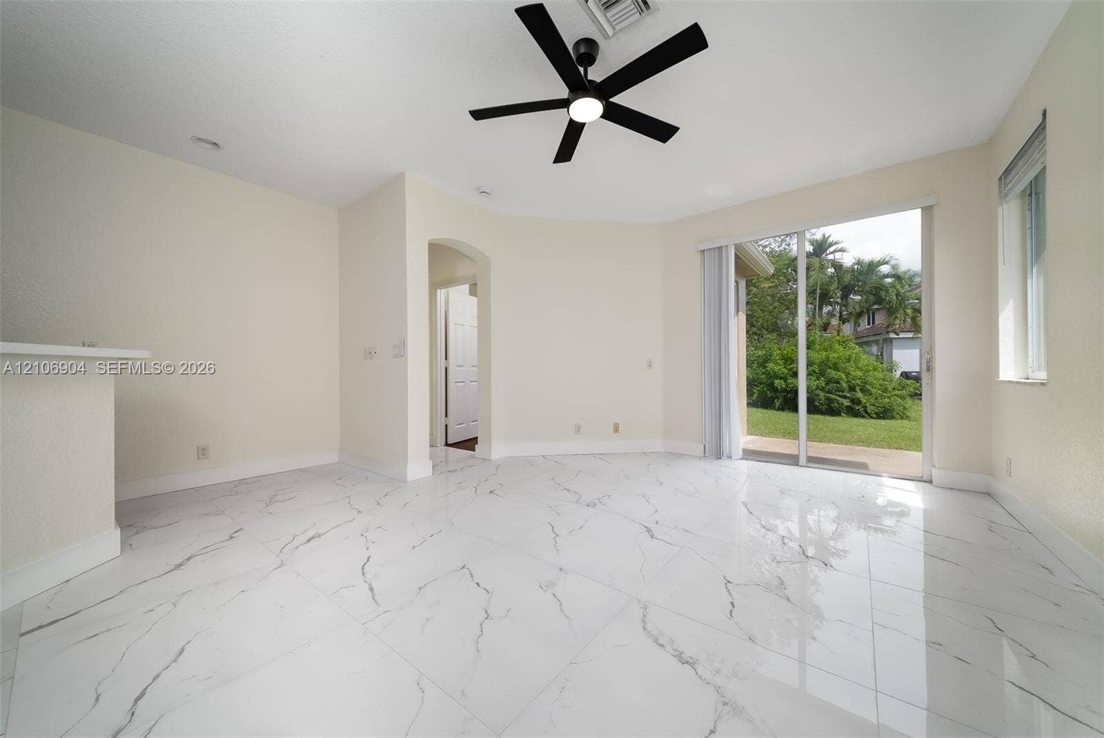 297 Conservation Drive, Weston, FL 33327 Interior space featuring large-format white tile flooring with dark veining, a matte black ceiling fan with integrated light, an arched entryway, and sliding glass doors