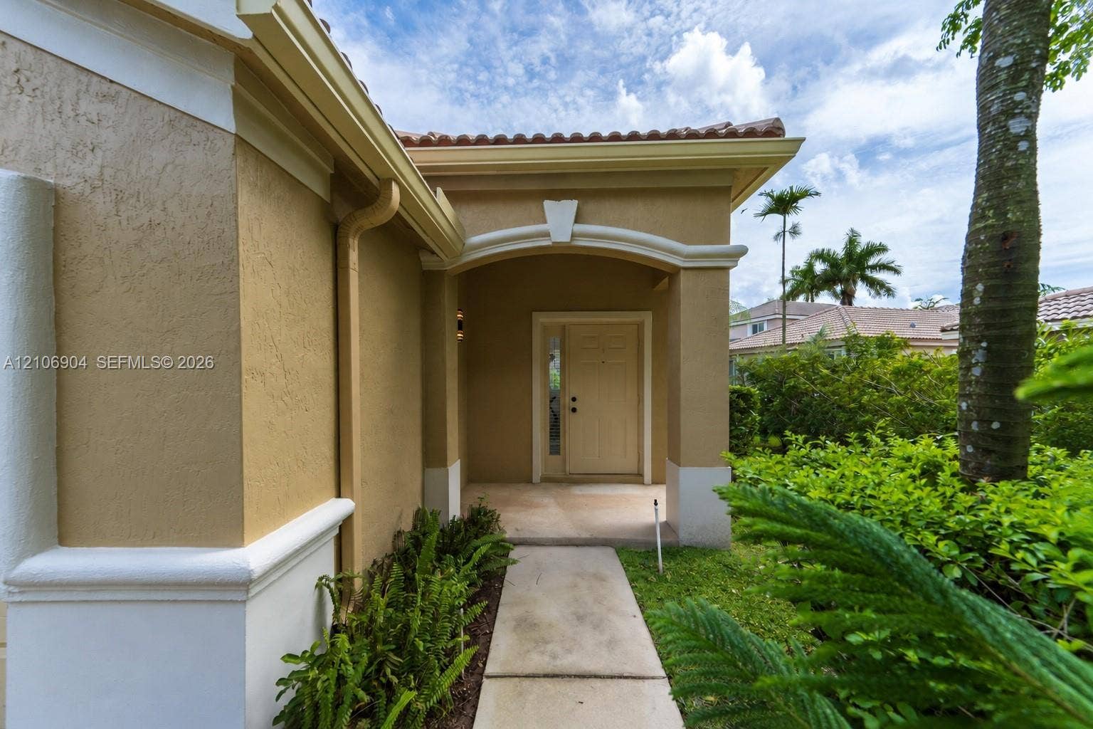 297 Conservation Drive, Weston, FL 33327 Stucco exterior with an arched covered entryway, a decorative keystone detail, a solid front door with sidelight, and a paved walkway