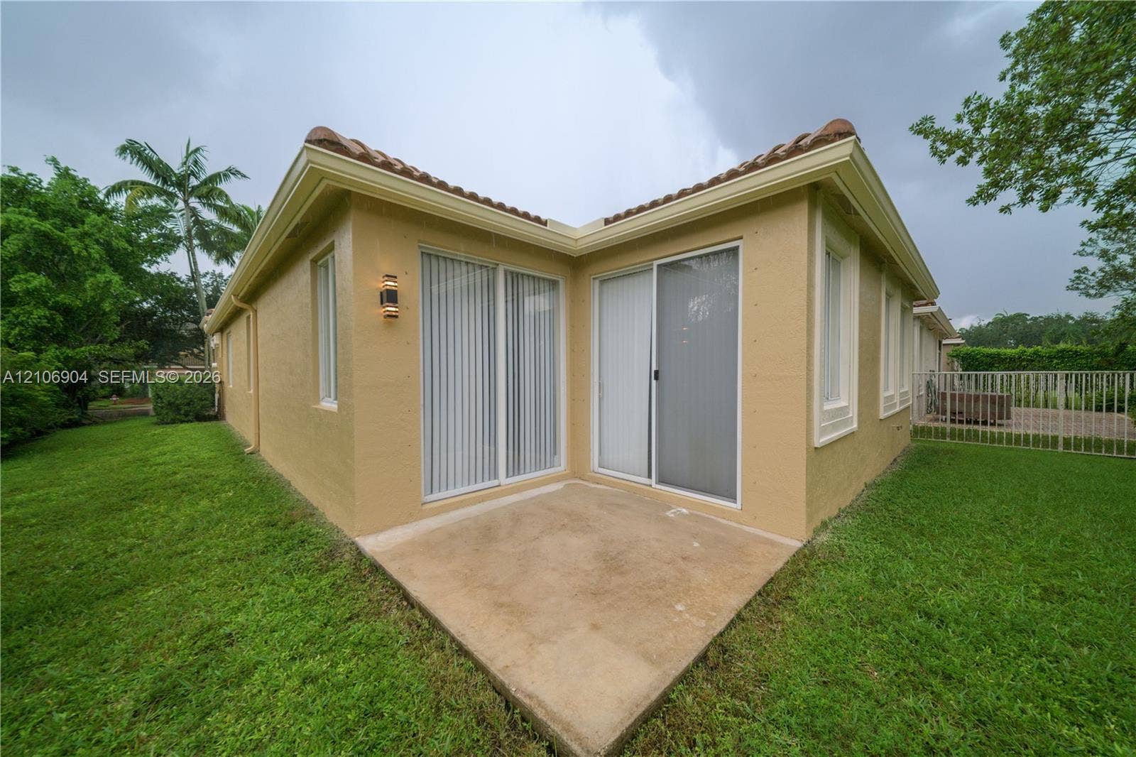297 Conservation Drive, Weston, FL 33327 Stucco exterior with a tiled roof, concrete patio, dual sliding glass doors, and exterior wall-mounted lighting