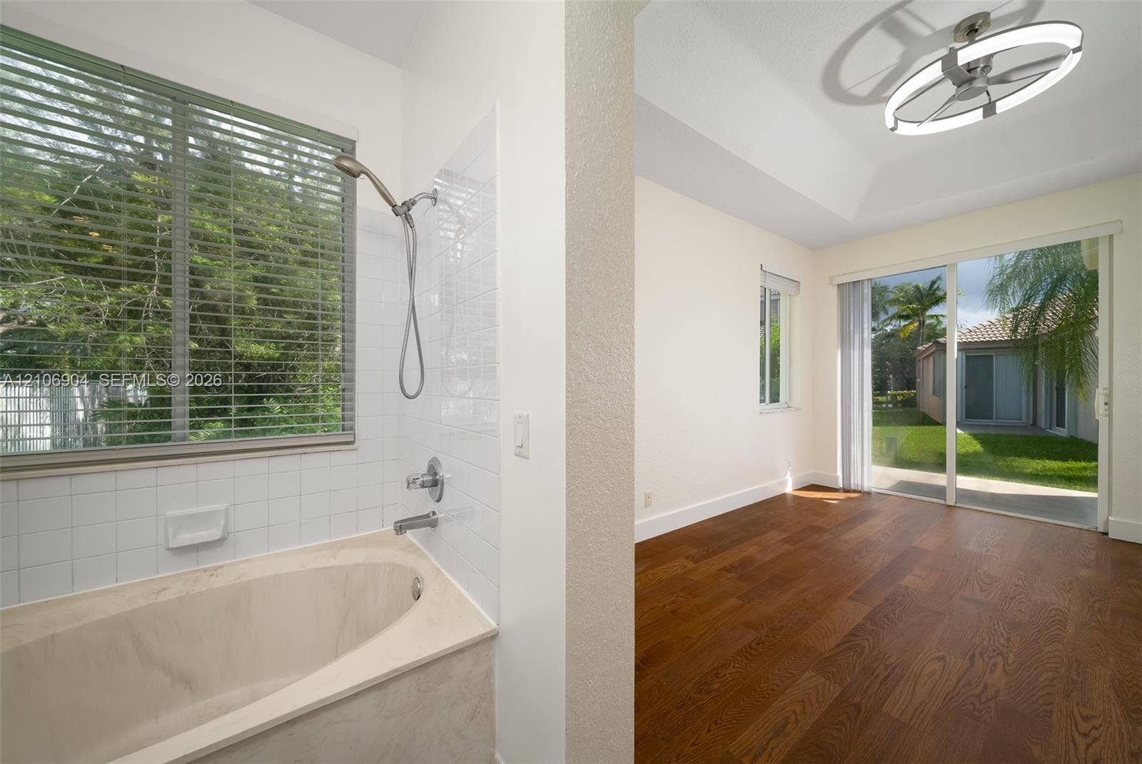 297 Conservation Drive, Weston, FL 33327 Soaking tub with tile surround, wood-finish flooring, tray ceiling, contemporary circular LED light fixture, and sliding glass doors