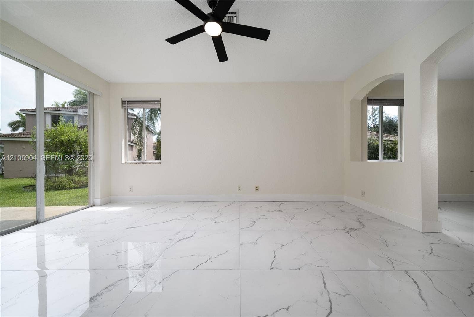 297 Conservation Drive, Weston, FL 33327 Large-format white tile flooring with grey veining, matte black ceiling fan with integrated lighting, glass sliding doors, and arched architectural wall detail