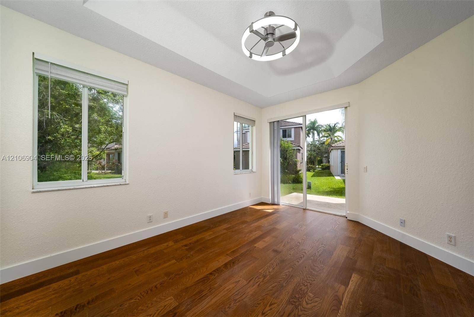 297 Conservation Drive, Weston, FL 33327 Interior space featuring wood-finish flooring, tray ceiling, integrated circular lighting fixture, two windows with blinds, and sliding glass doors