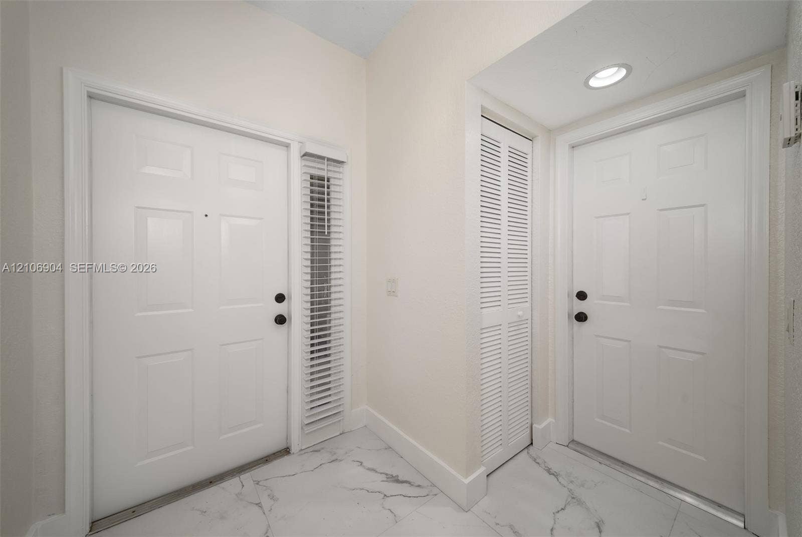297 Conservation Drive, Weston, FL 33327 Entryway featuring polished marble-style tile flooring, two six-panel doors with matte black hardware, vertical slatted window blinds, and a built-in louvered closet door with recessed ceiling lighting