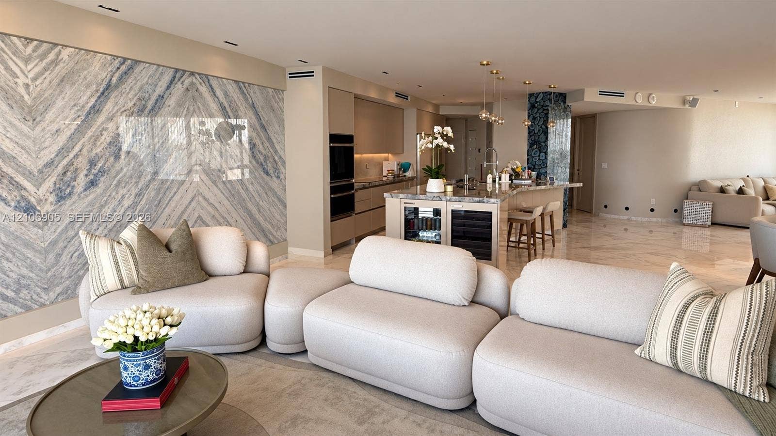 720 NE 69th Street, #10N, Miami, FL 33138 Open-concept living space featuring a floor-to-ceiling stone accent wall, natural stone flooring, an expansive kitchen island with a built-in beverage center, and recessed lighting