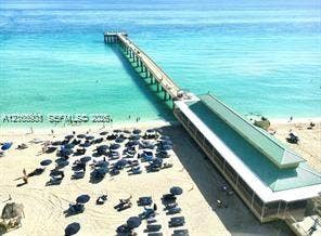 Aerial perspective of a coastal pier with a pitched metal roof, sandy beachfront, and direct ocean access