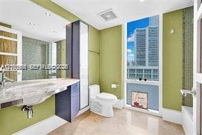 Wall-mounted stone-surface vanity with undermount basin, floor-to-ceiling cabinetry, recessed lighting, and expansive floor-to-ceiling windows