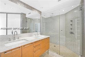 Dual-sink vanity with light-tone cabinetry and stone countertop, complemented by a walk-in glass-enclosed shower featuring multi-head wall-mounted fixtures