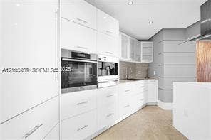 Modern kitchen featuring high-gloss white cabinetry, integrated stainless steel appliances, recessed lighting, and wood-finish flooring