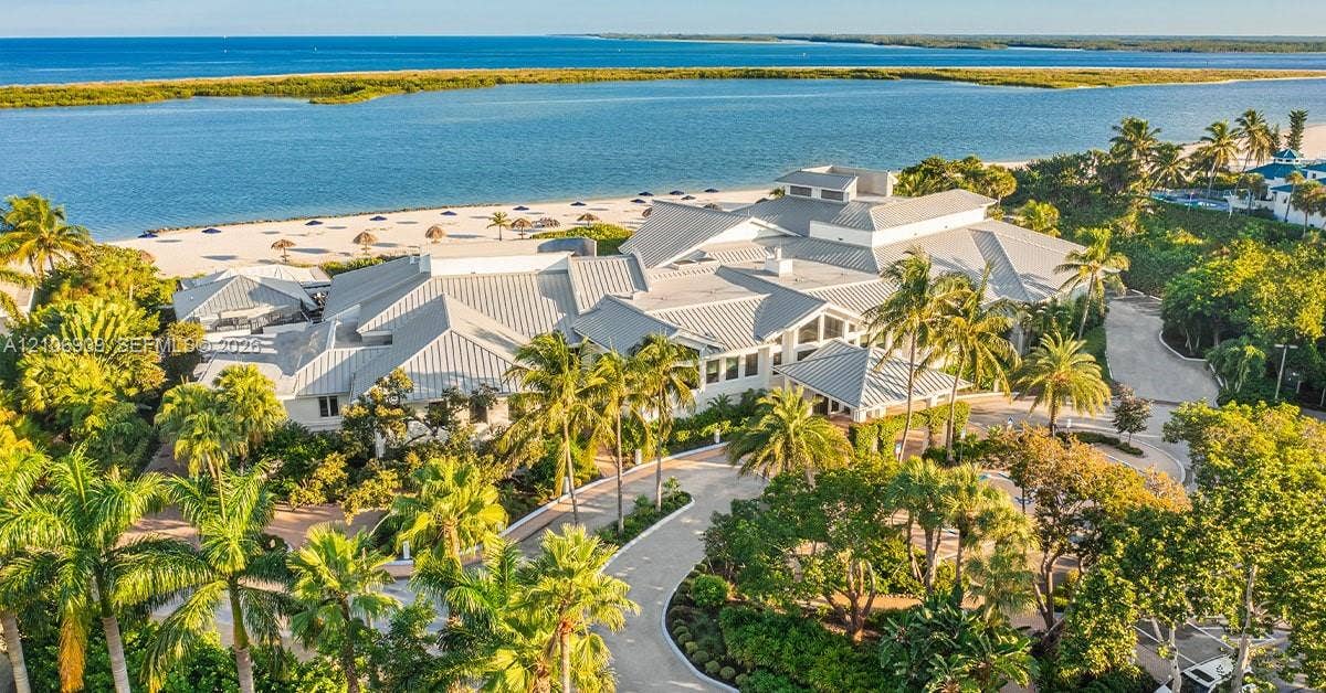 331 Wild Orchid Lane, Marco Island, Marco Island, FL 34145 Waterfront estate featuring a multi-gabled metal roof, mature tropical landscaping, paved circular driveway, and direct access to a sandy beach