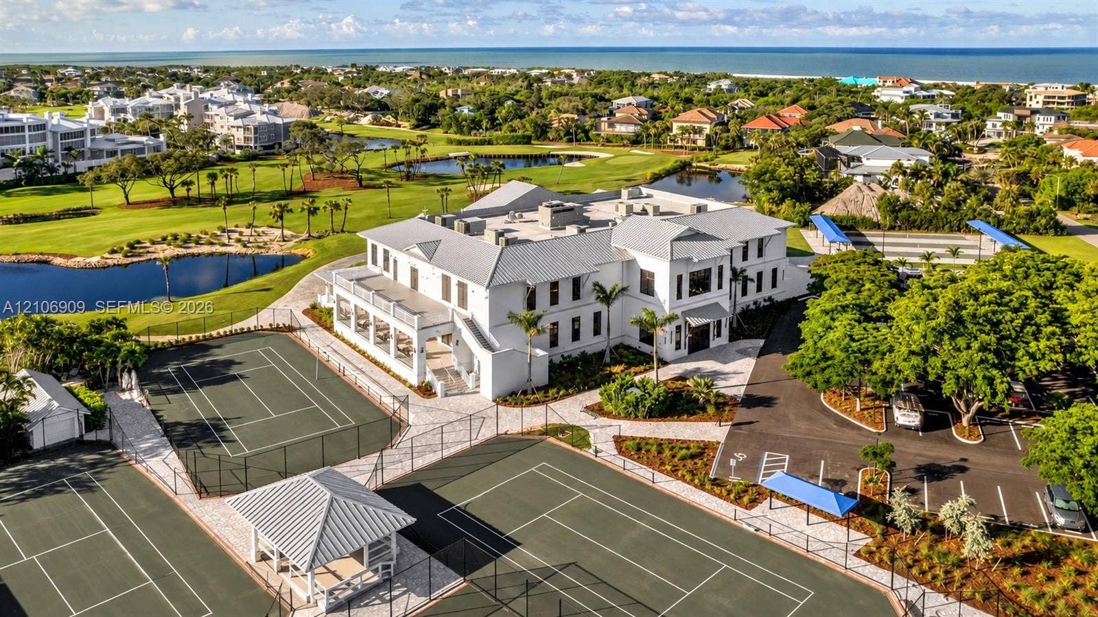 331 Wild Orchid Lane, Marco Island, Marco Island, FL 34145 Aerial perspective of a white multi-story exterior featuring multiple tennis courts, a covered pavilion, asphalt parking, and manicured landscaping