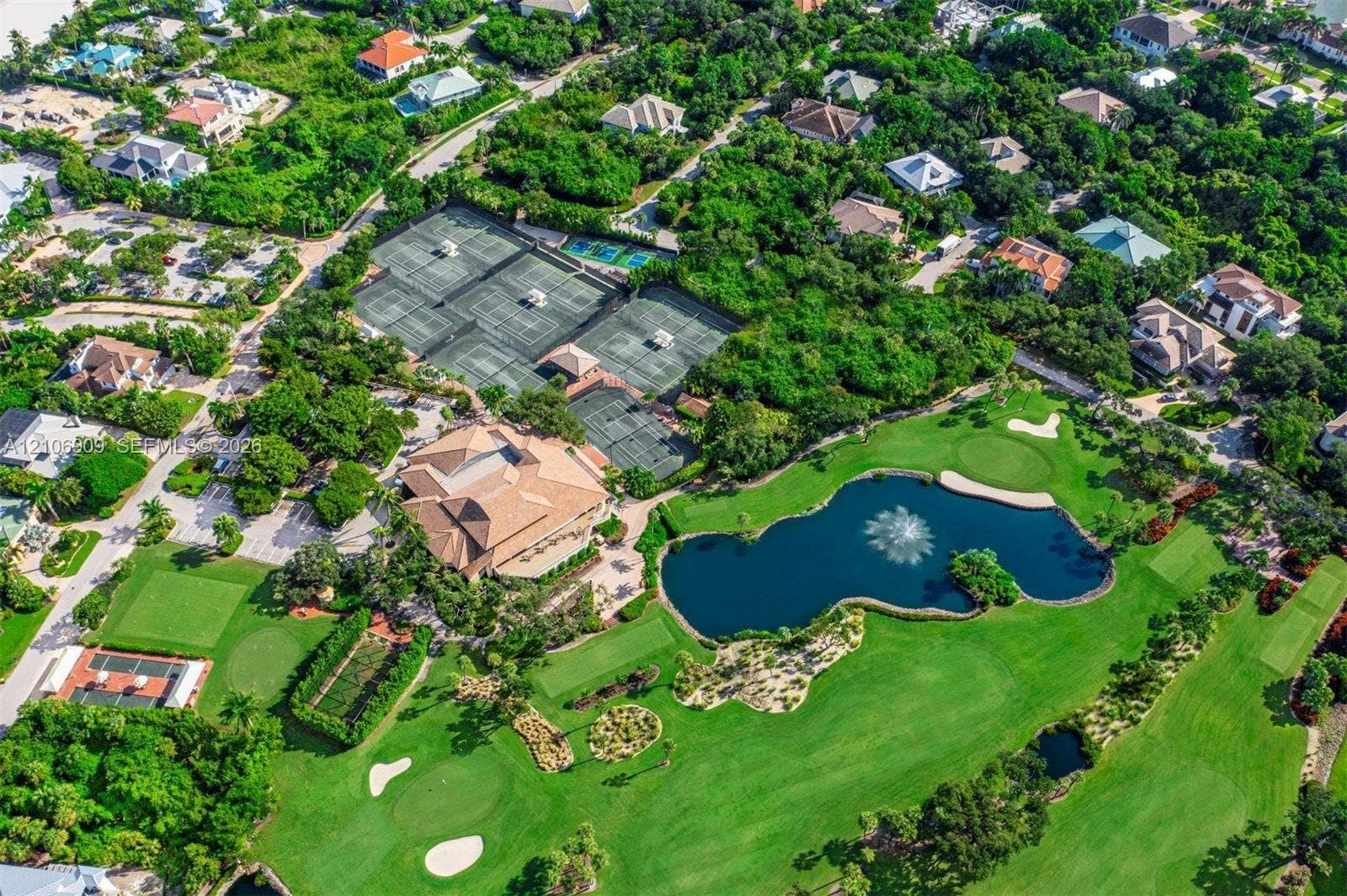 331 Wild Orchid Lane, Marco Island, Marco Island, FL 34145 Aerial perspective featuring multiple tennis courts, a central clubhouse with a tile roof, an expansive golf course, and a large water feature with an integrated fountain