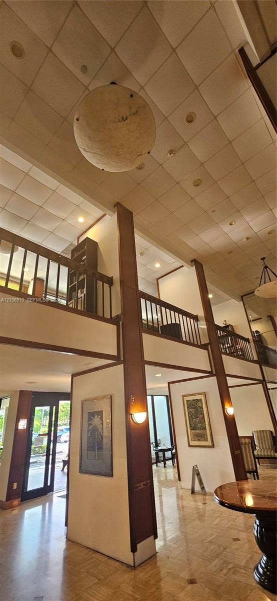 Double-height atrium featuring polished stone flooring, exposed structural wood beams, a suspended globe pendant light, and a wooden mezzanine railing