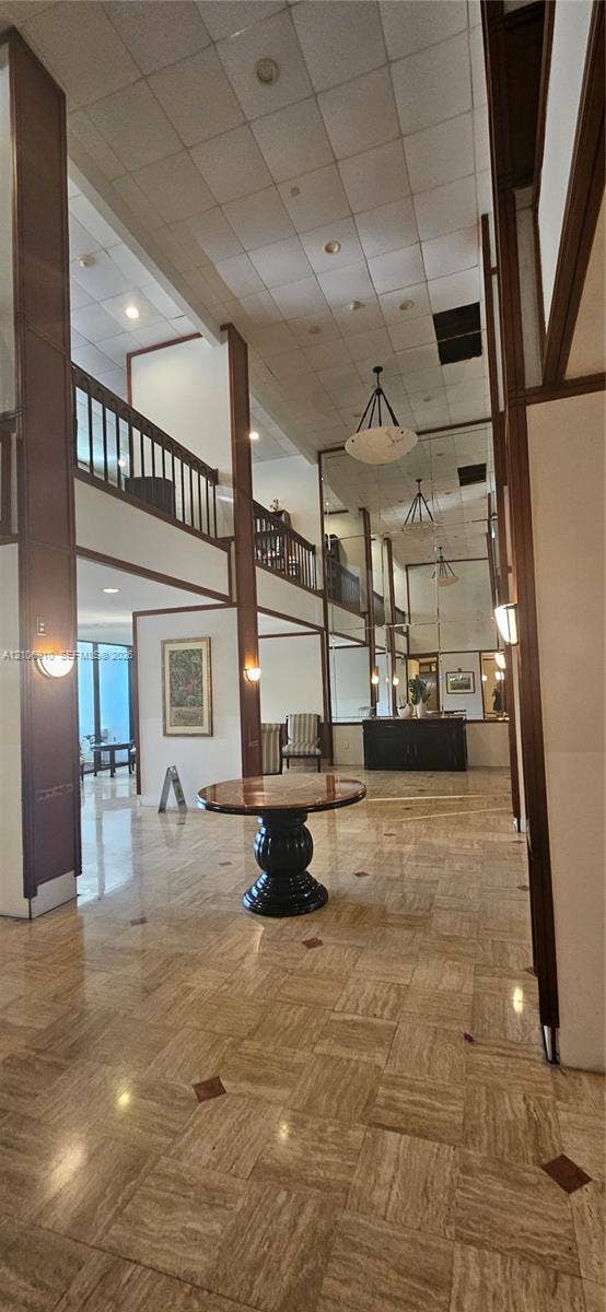 Double-height entry featuring polished stone flooring with decorative inlays, full-height wall mirrors, custom wood-trim detailing, and a mezzanine-level balcony railing