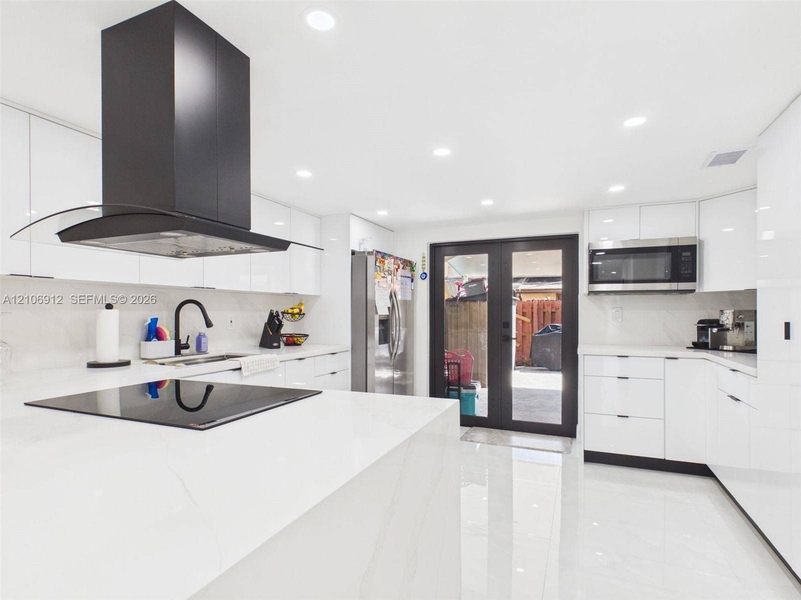 1142 W 42nd Street, #19, Hialeah, FL 33012 Modern kitchen featuring high-gloss white cabinetry, expansive stone countertops, a stainless steel built-in microwave, a matte black range hood, and glass-paneled double doors