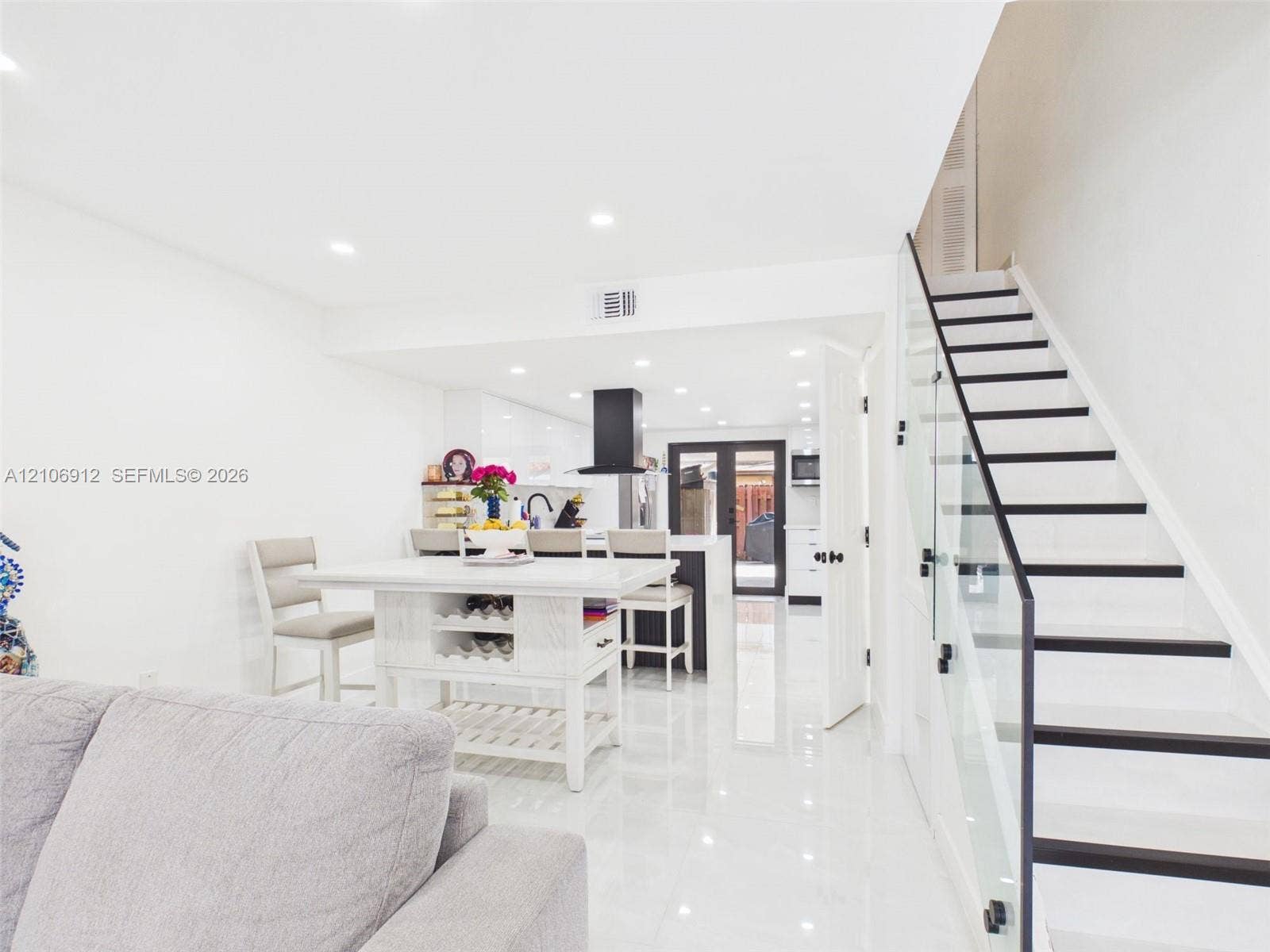 1142 W 42nd Street, #19, Hialeah, FL 33012 Staircase featuring glass paneling and dark-finished treads, high-gloss tile flooring, recessed ceiling lighting, and a kitchen area with a matte black range hood